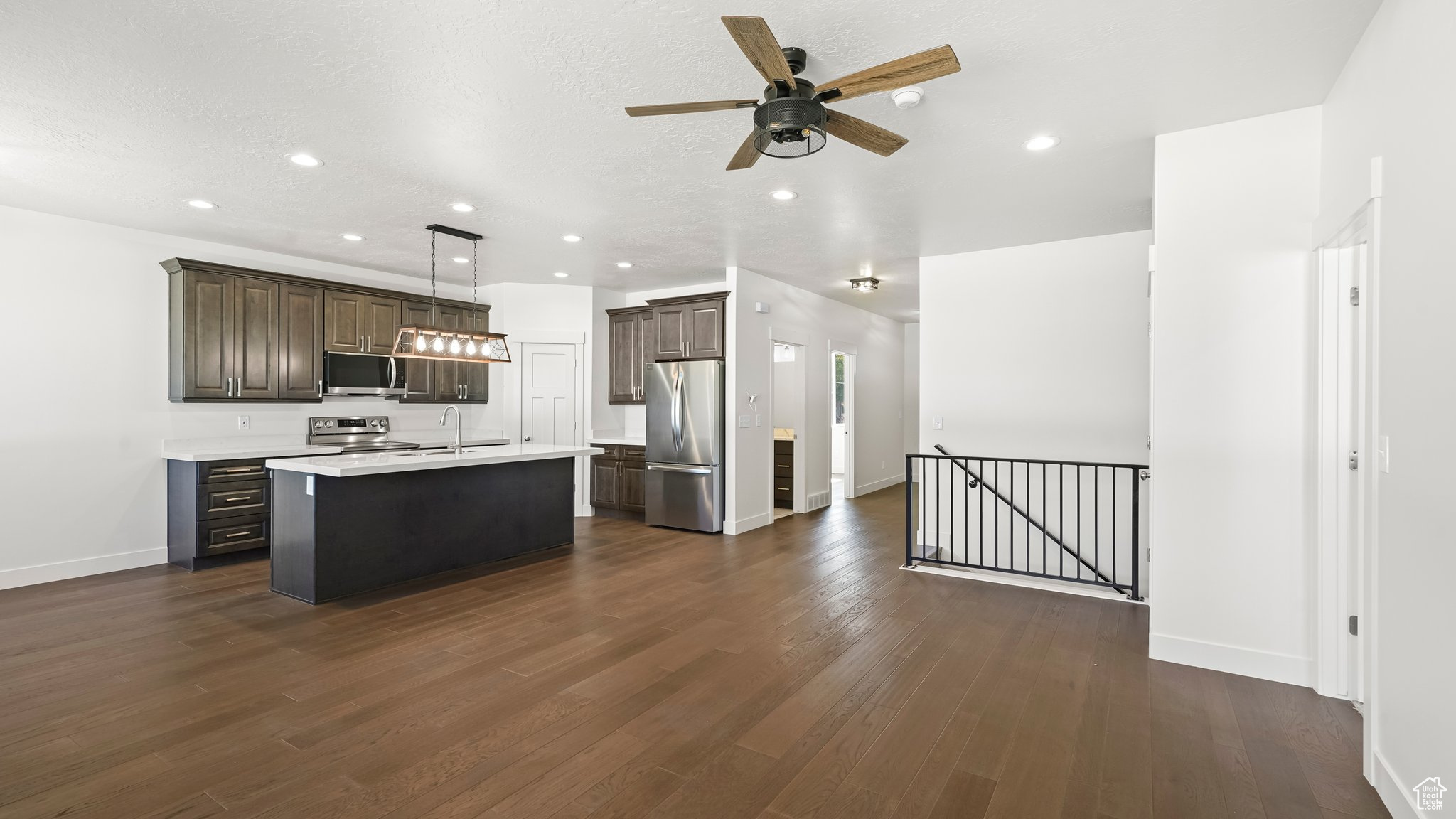 Kitchen with dark hardwood / wood-style floors, an island with sink, stainless steel appliances, and hanging light fixtures