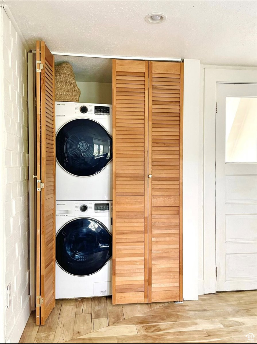 Laundry room featuring light hardwood / wood-style flooring, stacked washer / dryer, and a textured ceiling