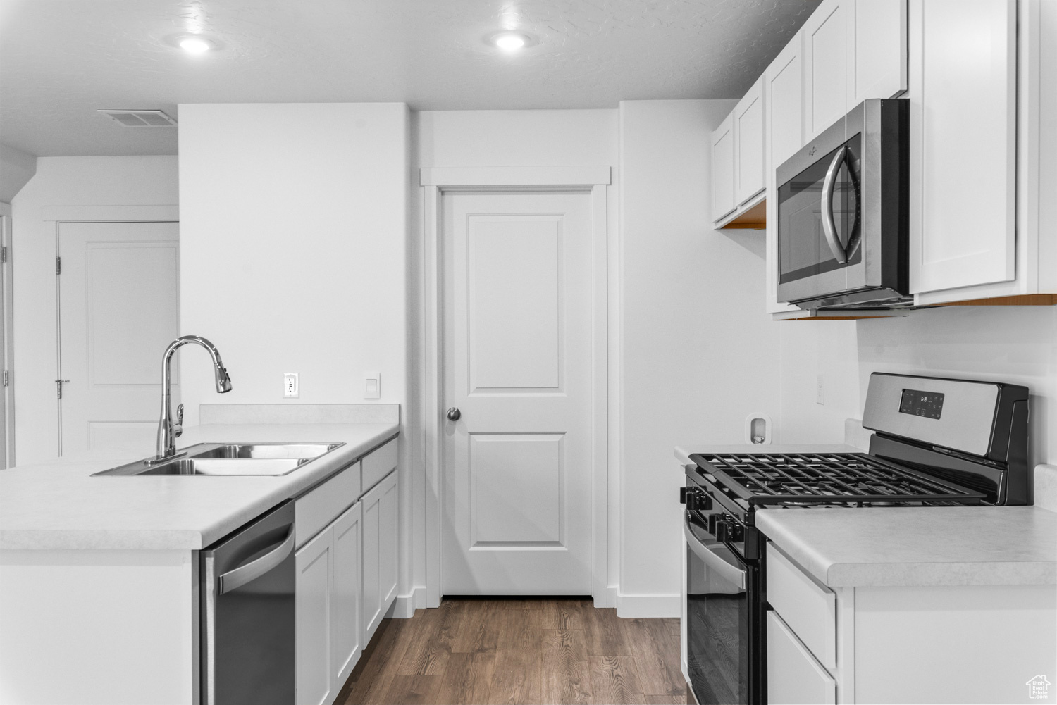 Kitchen with white cabinets, sink, stainless steel appliances, and dark wood-type flooring