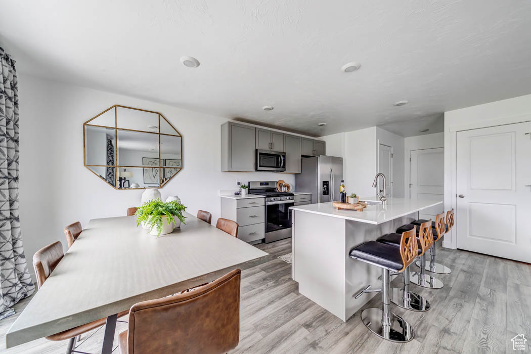 Kitchen with sink, appliances with stainless steel finishes, light hardwood / wood-style floors, gray cabinetry, and a breakfast bar