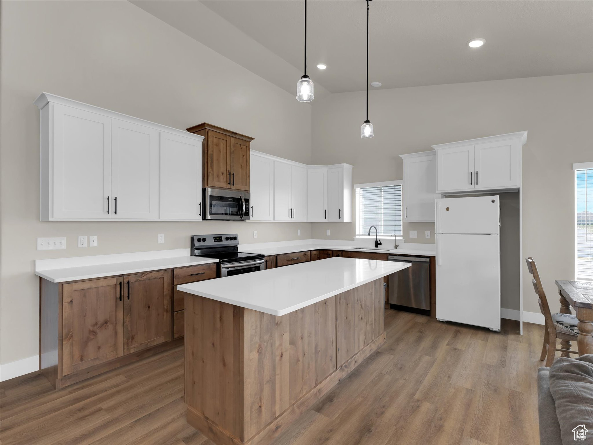 Kitchen featuring decorative light fixtures, light hardwood / wood-style flooring, stainless steel appliances, white cabinets, and a center island