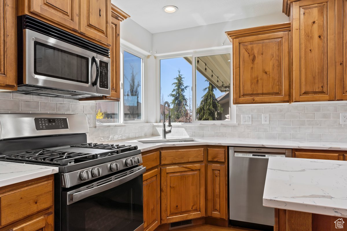 Kitchen with backsplash, stainless steel appliances, sink, and light stone counters
