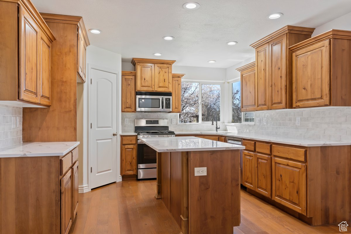 Kitchen with light hardwood / wood-style flooring, a center island, backsplash, and stainless steel appliances