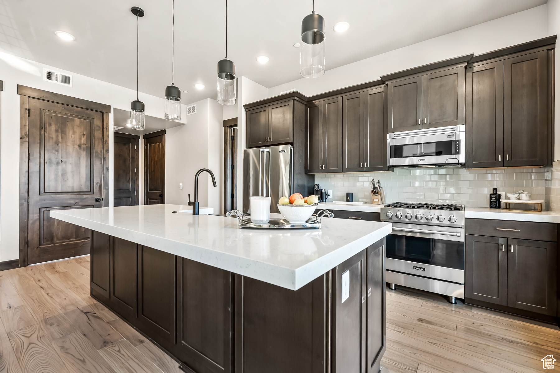 Kitchen featuring premium appliances, light hardwood / wood-style floors, tasteful backsplash, dark brown cabinets, and pendant lighting