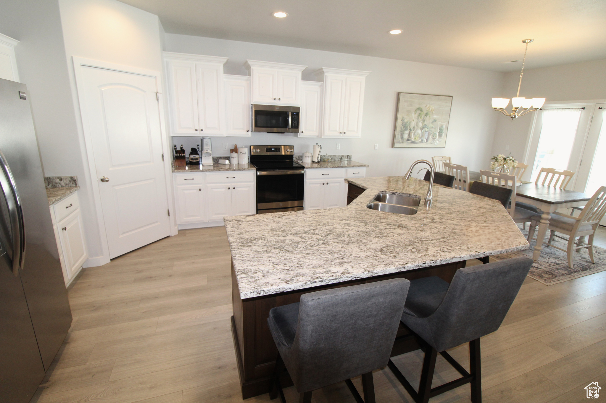 Kitchen with pendant lighting, white cabinets, light wood-type flooring, stainless steel appliances, and sink
