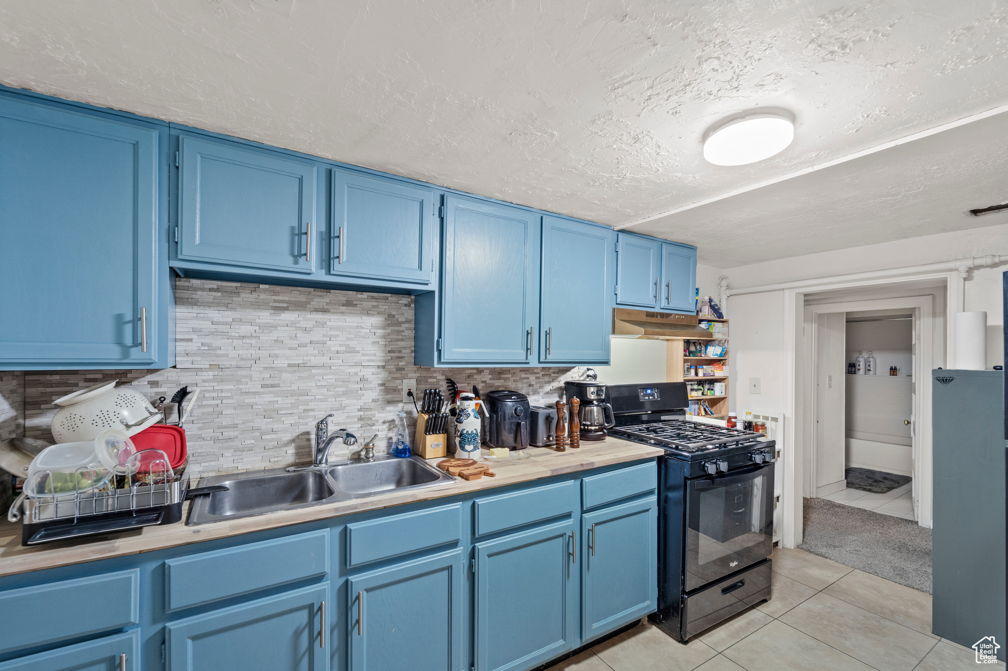 Kitchen with backsplash, blue cabinetry, sink, light tile floors, and black gas range