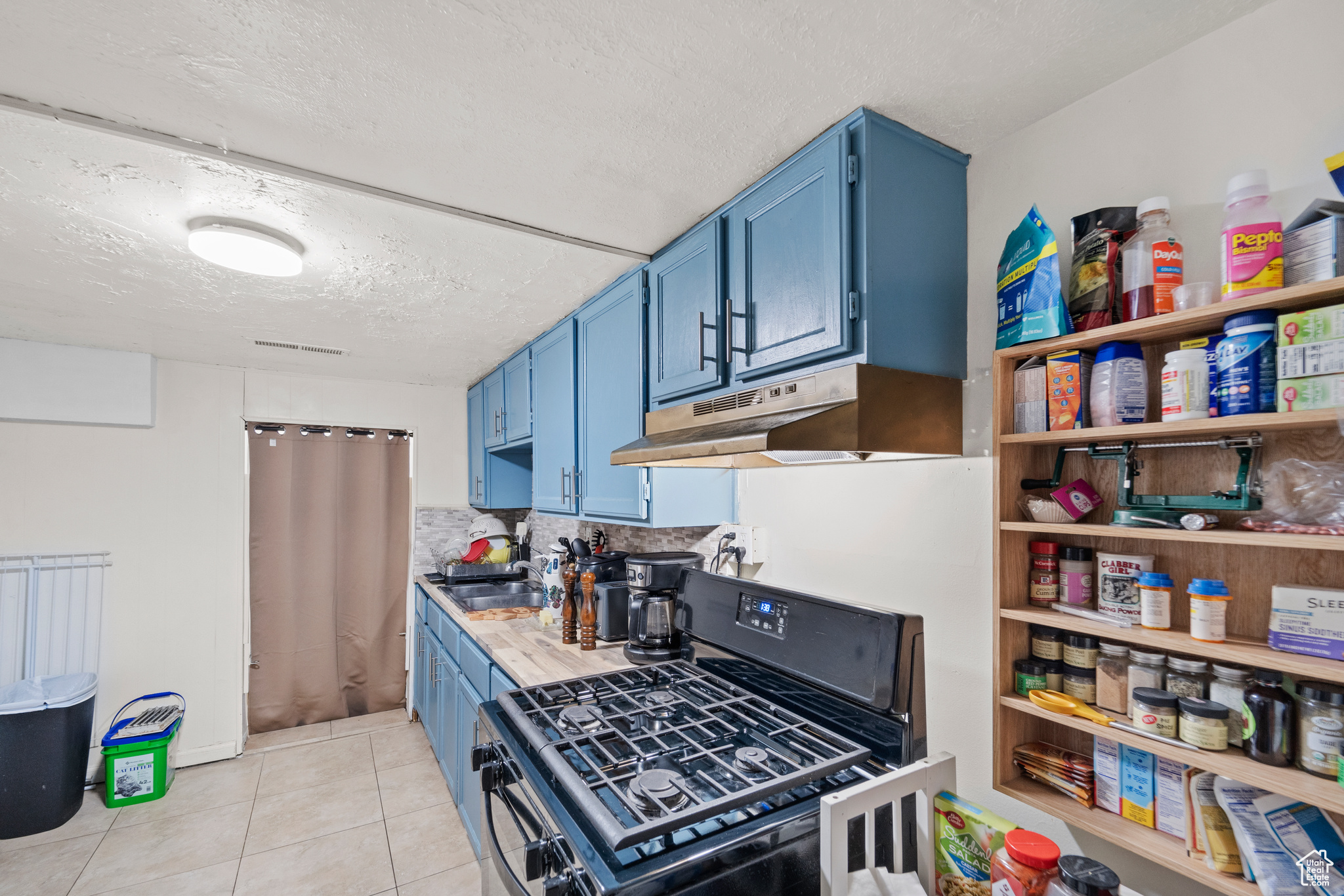 Kitchen featuring a textured ceiling, blue cabinets, light tile flooring, and range with gas stovetop
