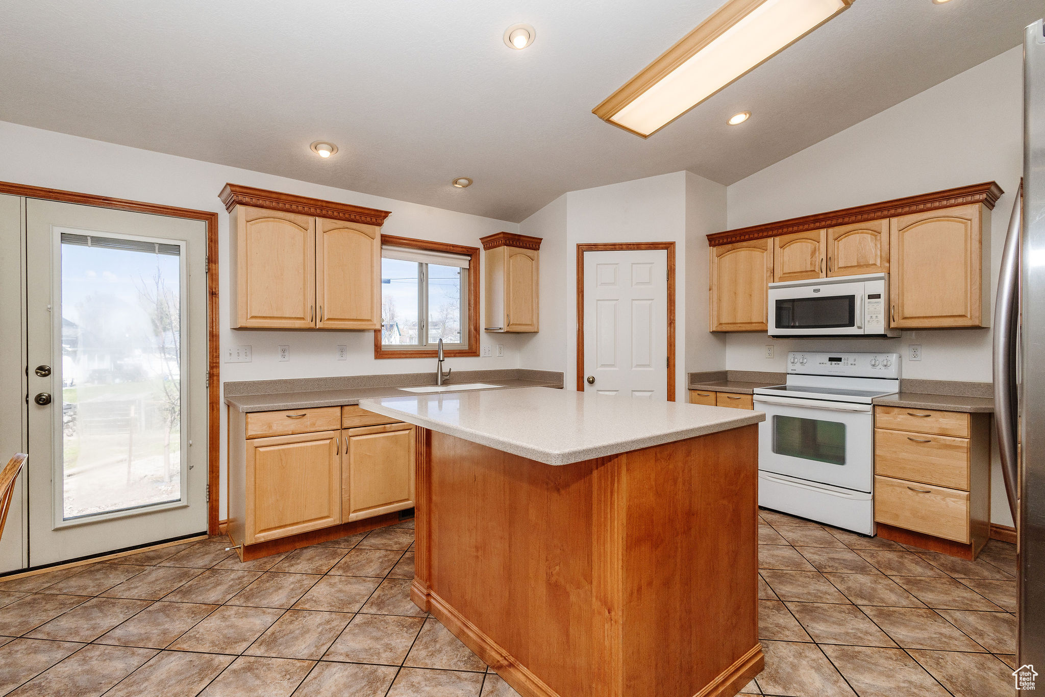 Kitchen with island, light tile floors, white appliances, and vaulted ceiling.  Open to semi-formal dining that open to great room.