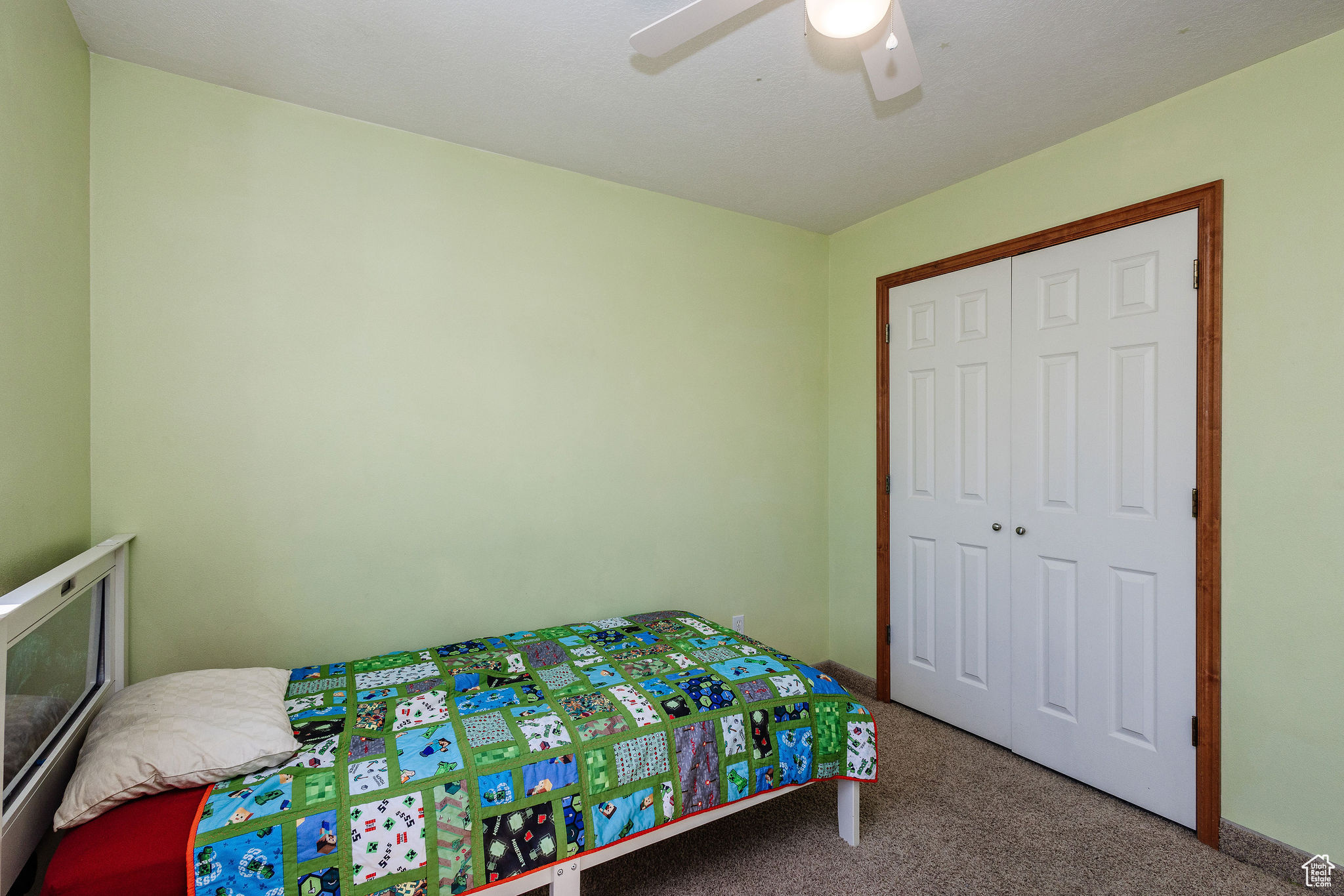 Bedroom with light colored carpet, ceiling fan, and a closet trimmed with oak wood stain.