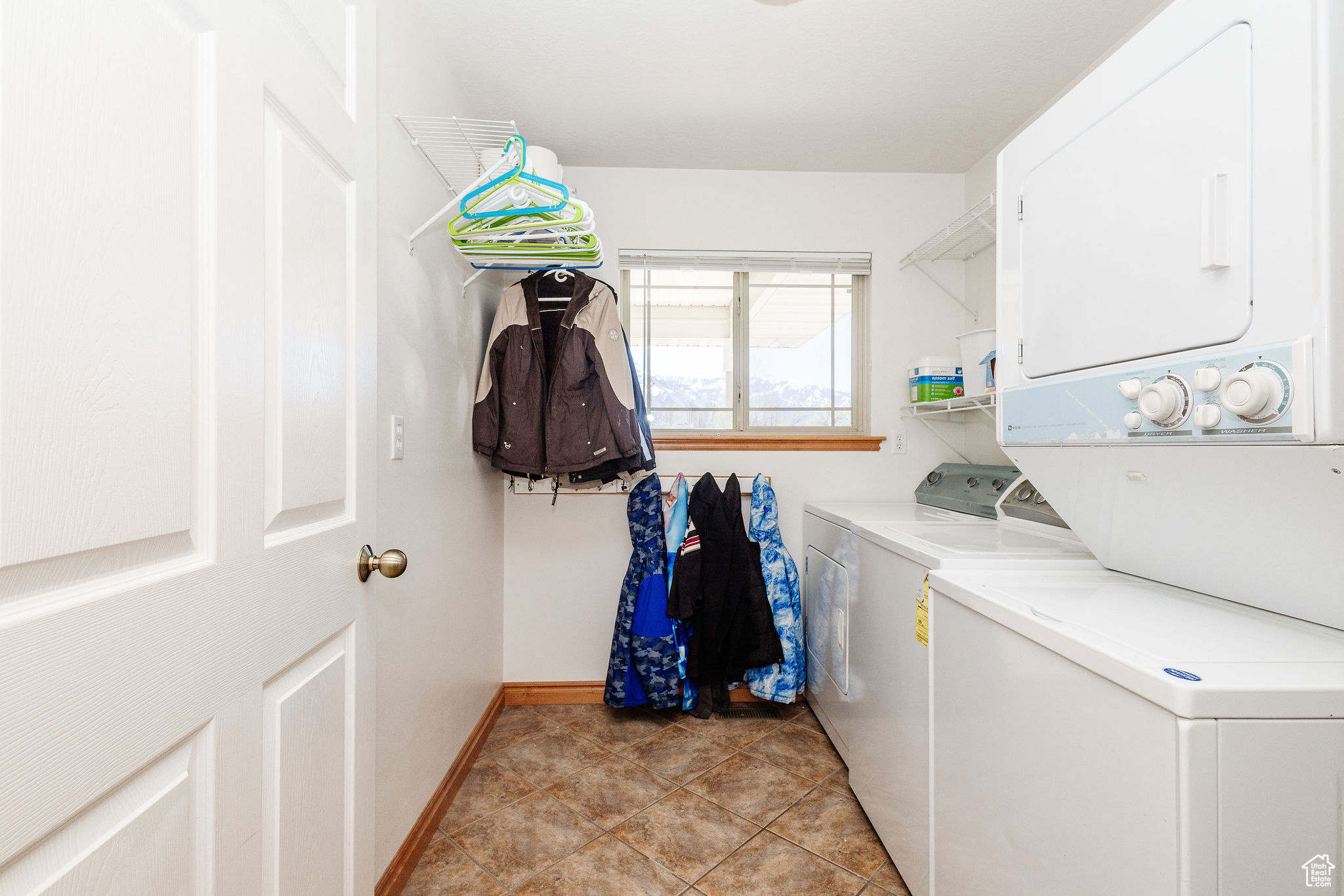 Laundry area featuring light tile floors and stacked washing maching and dryer