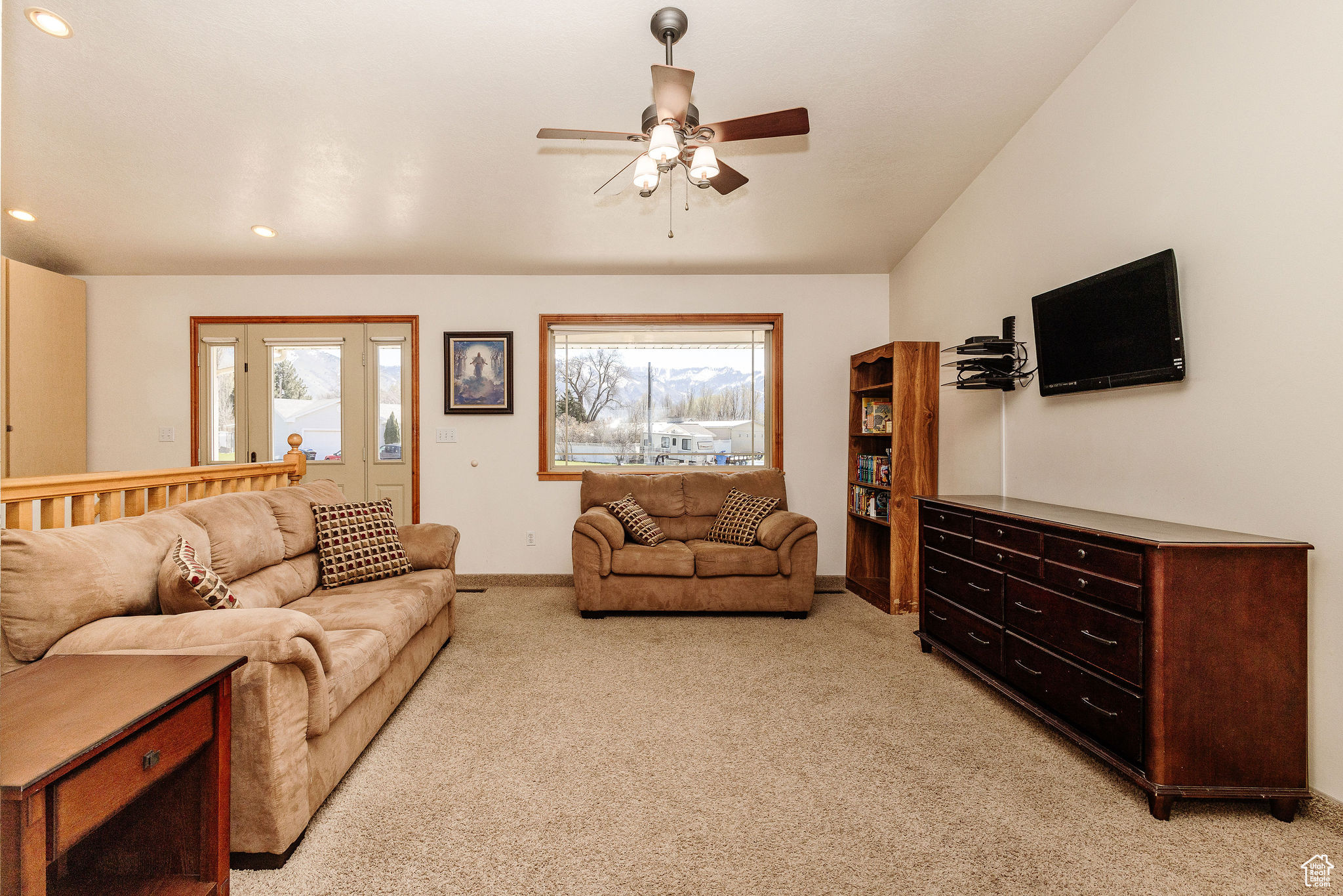Carpeted great room with ceiling fan, vaulted ceiling and mounted TV. Open to semi-formal dining into kitchen.