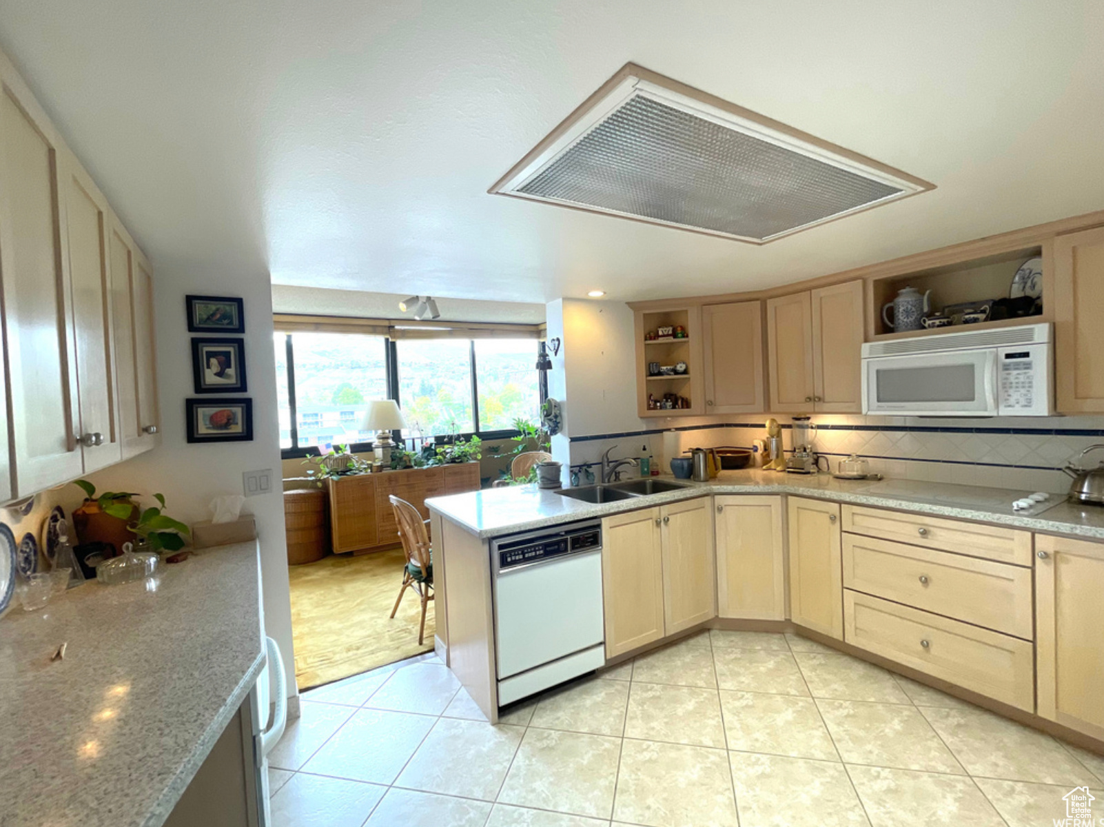 Kitchen featuring kitchen peninsula, backsplash, white appliances, light tile flooring, and sink