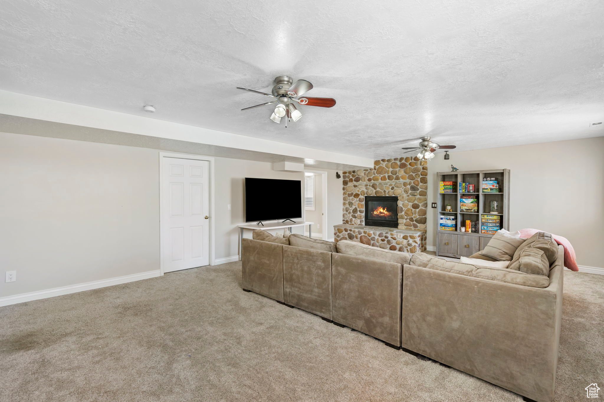 Living room featuring a stone fireplace, light colored carpet, ceiling fan, and a textured ceiling