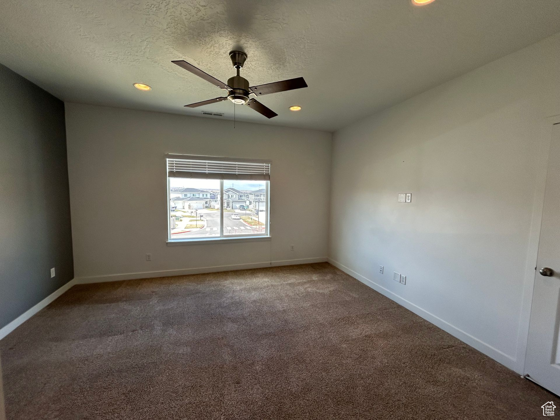 Spare room featuring a textured ceiling, dark colored carpet, and ceiling fan