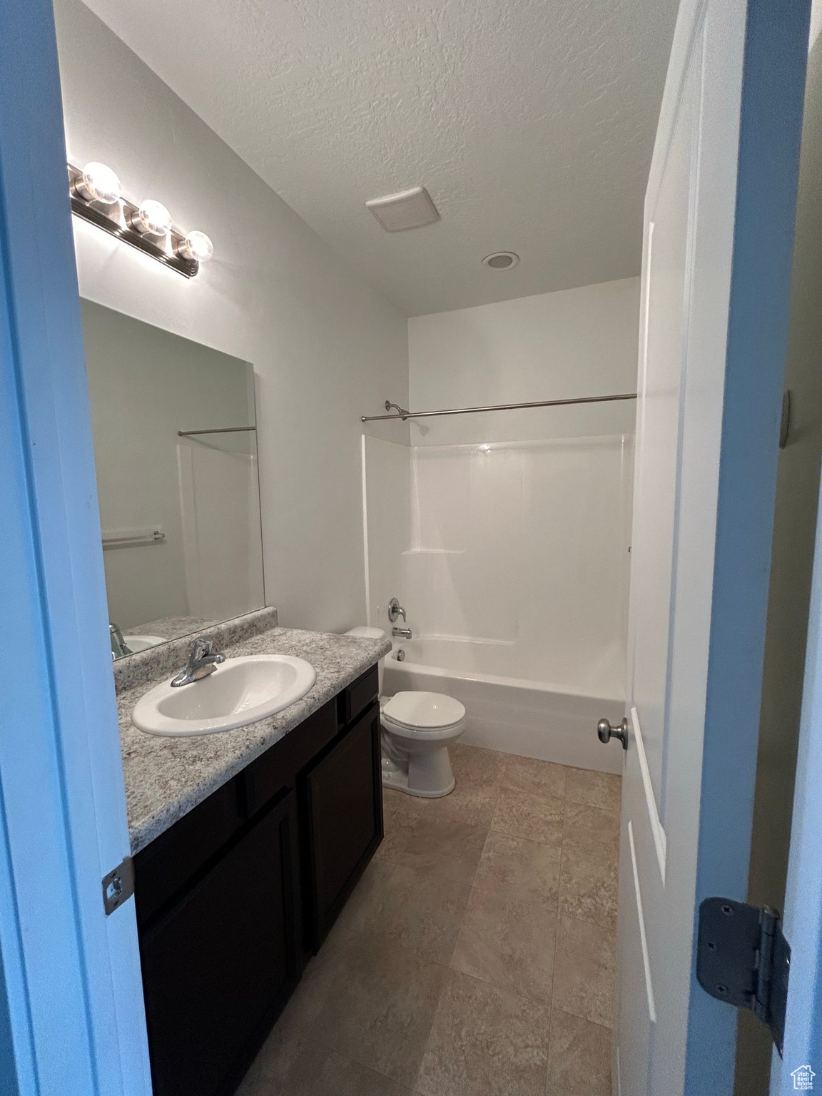 Full bathroom with bathing tub / shower combination, toilet, a textured ceiling, vanity, and tile floors