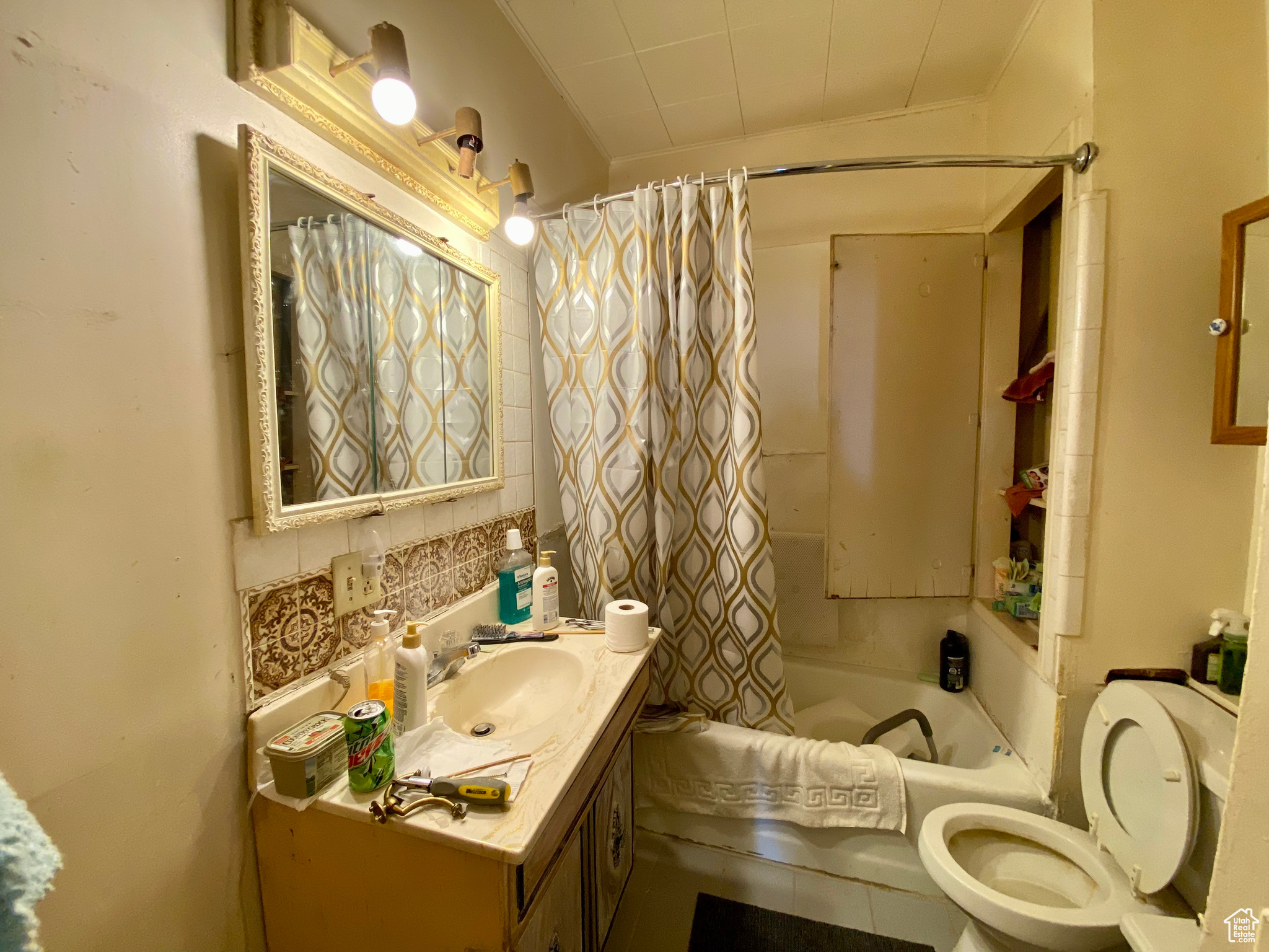 Full bathroom with vanity, backsplash, shower / bath combination with curtain, and toilet