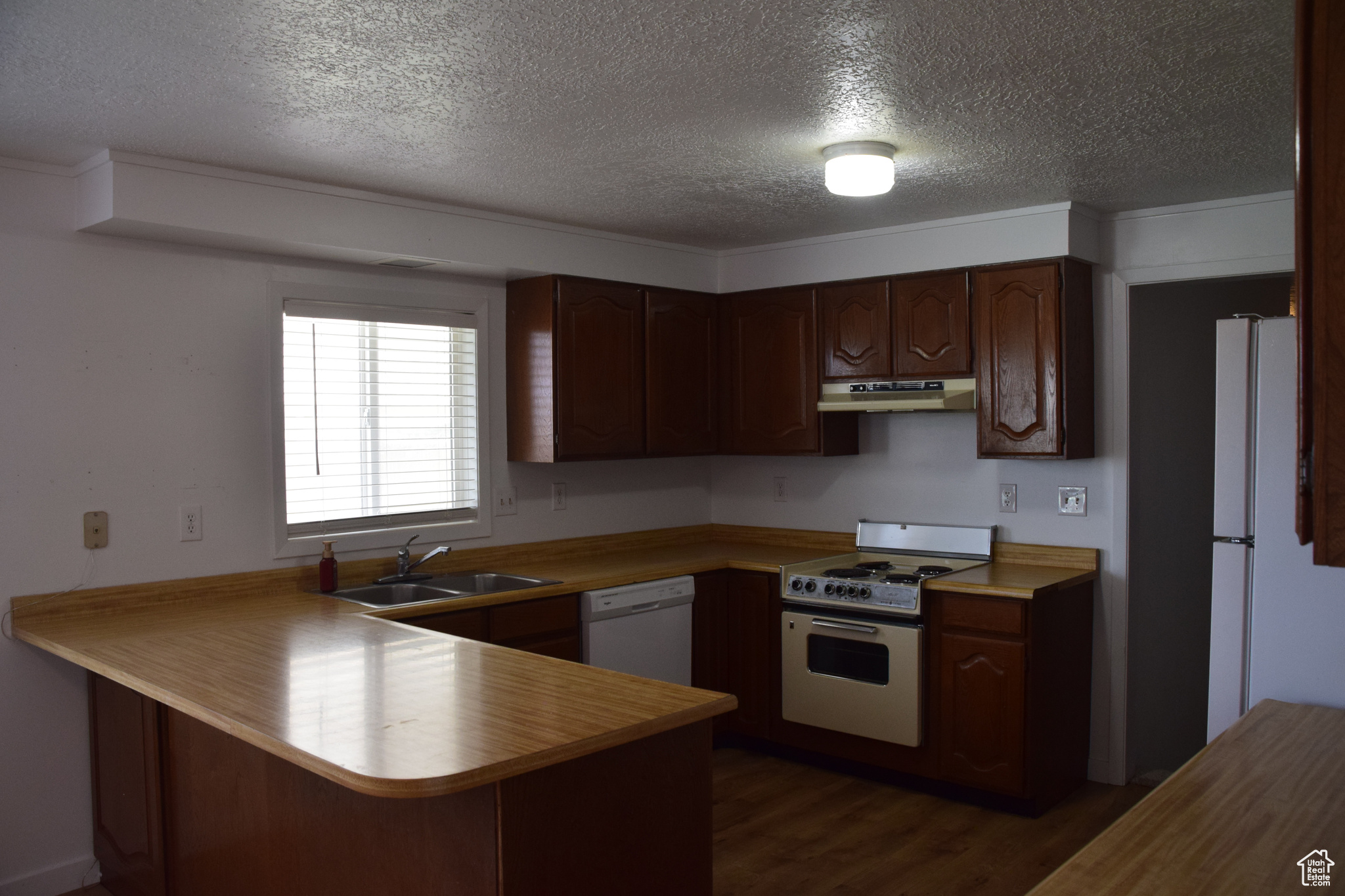 Kitchen featuring a textured ceiling, sink, white appliances, dark wood-type flooring, and kitchen peninsula