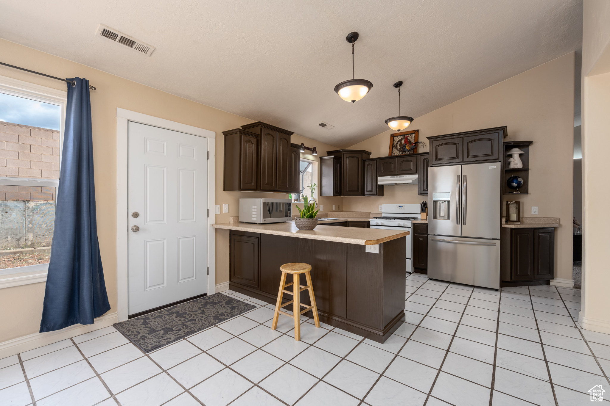 Kitchen featuring a healthy amount of sunlight, lofted ceiling, white appliances, and a kitchen bar