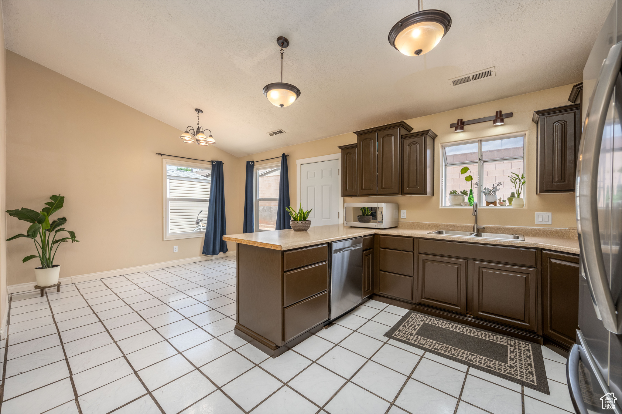 Kitchen with kitchen peninsula, appliances with stainless steel finishes, vaulted ceiling, sink, and pendant lighting