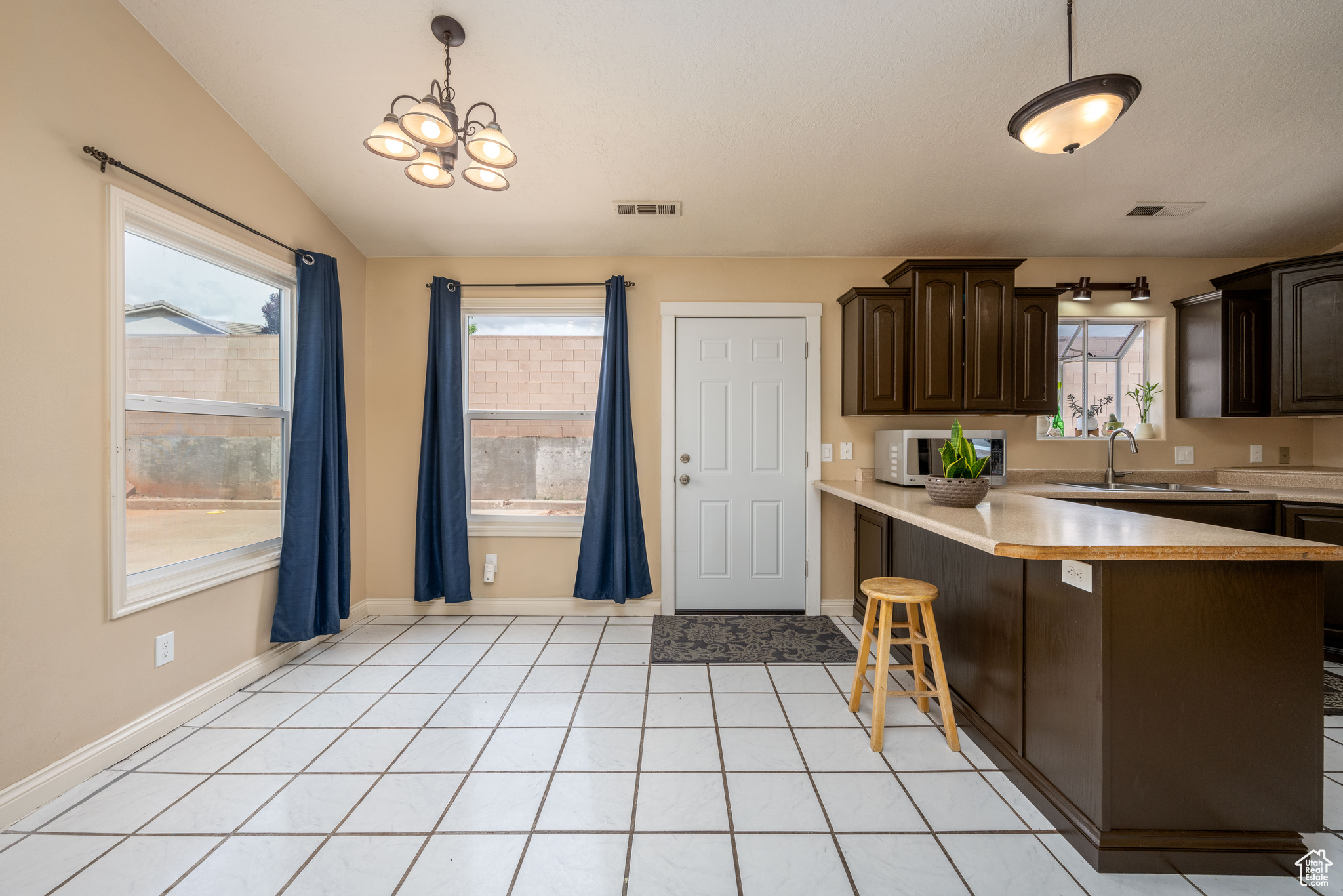 Kitchen featuring decorative light fixtures, a breakfast bar, sink, vaulted ceiling, and light tile floors
