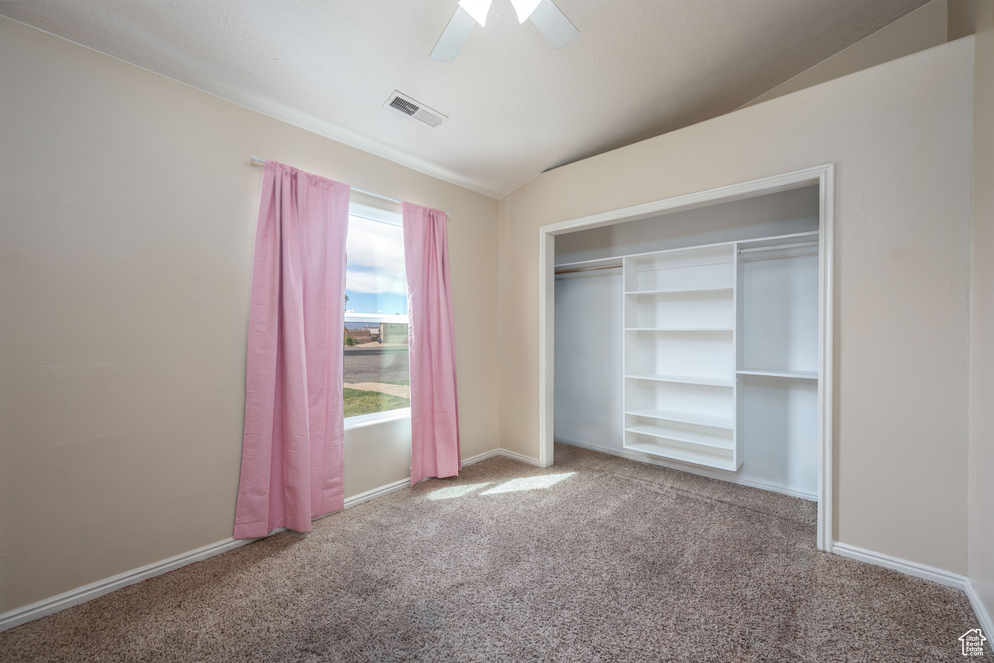 Unfurnished bedroom with a closet, ceiling fan, vaulted ceiling, and light carpet
