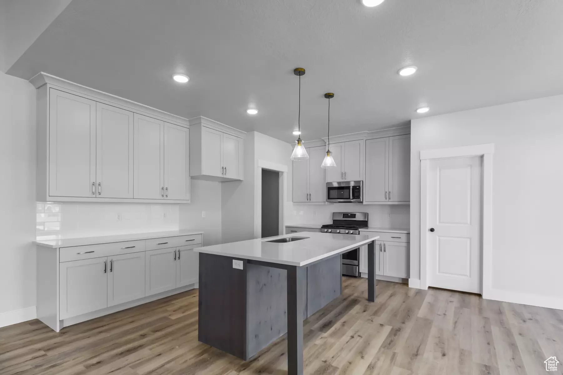 Kitchen featuring decorative light fixtures, appliances with stainless steel finishes, light hardwood / wood-style flooring, an island with sink, and a breakfast bar