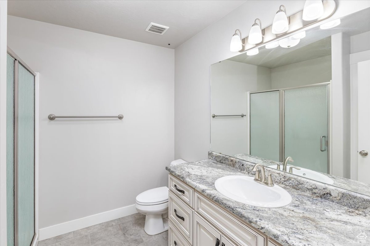 Bathroom featuring a shower with door, tile floors, toilet, and large vanity