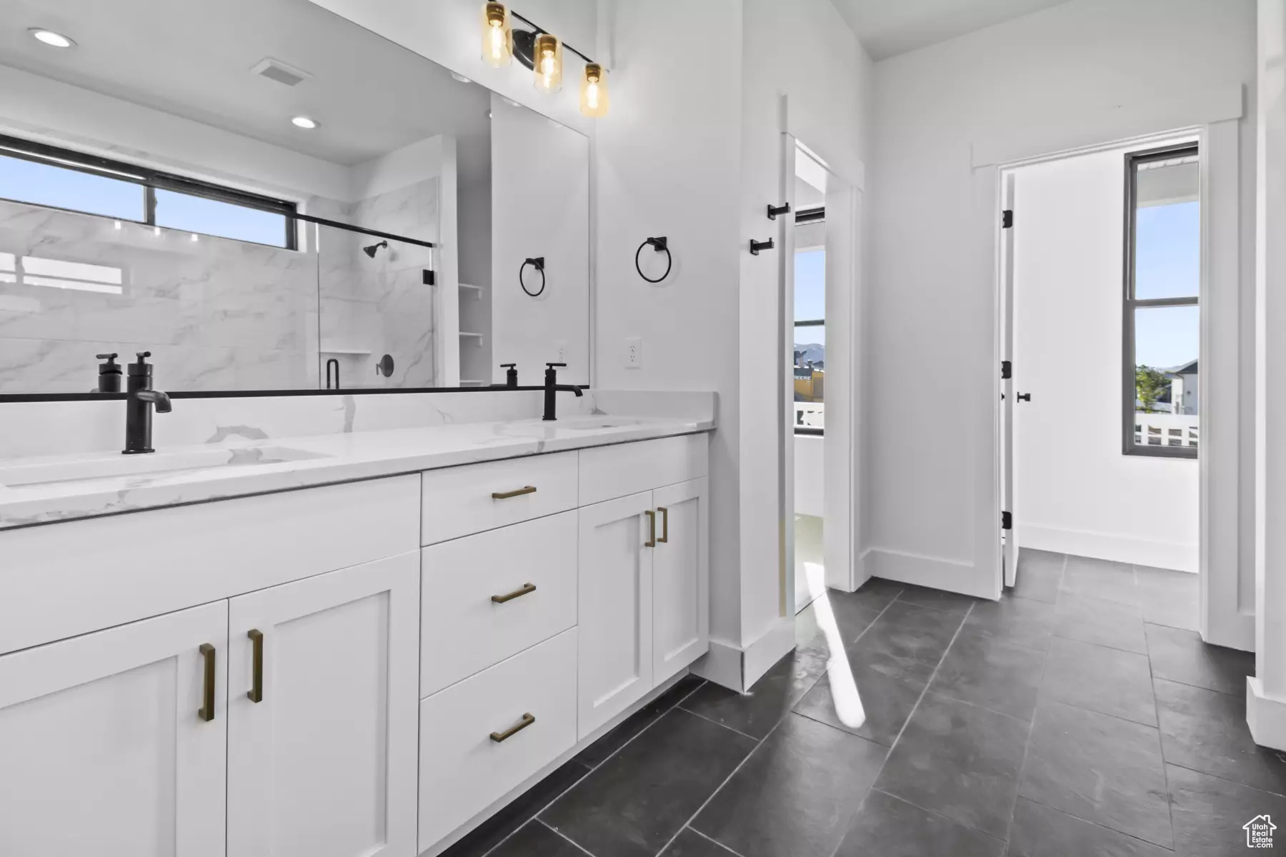 Bathroom with plenty of natural light, a shower with shower door, double vanity, and tile flooring