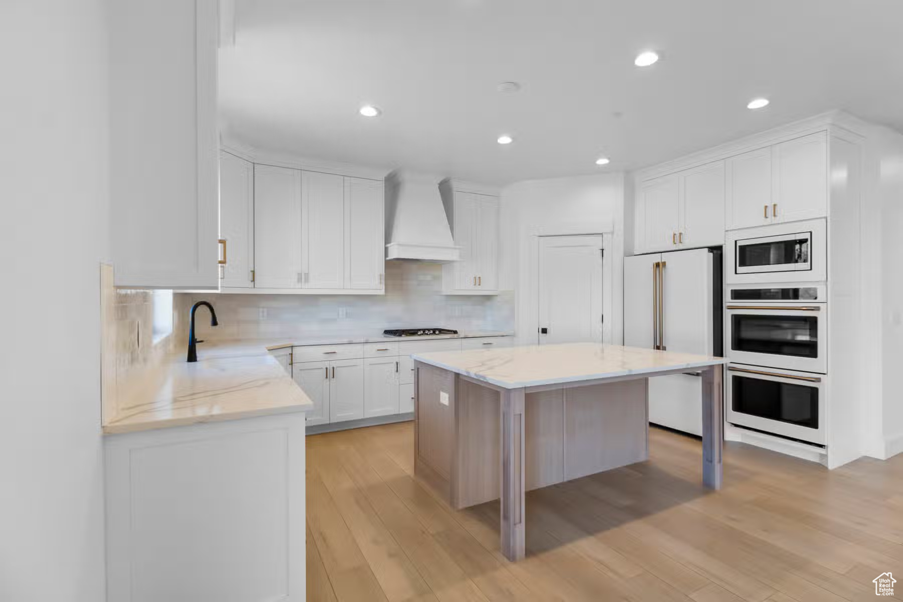 Kitchen featuring premium range hood, built in appliances, light hardwood / wood-style flooring, and light stone countertops