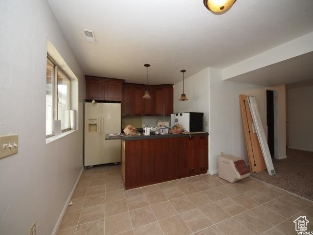 Lower level Kitchen with decorative light fixtures, white fridge with ice dispenser, kitchen peninsula, and light tile floors