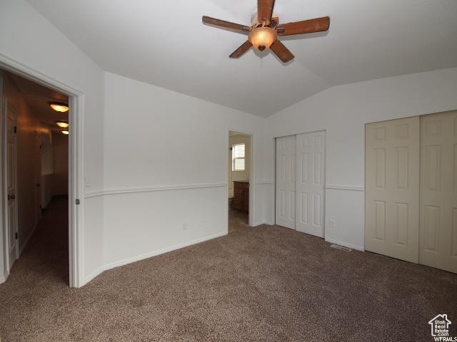 Upstairs  bedroom featuring ceiling fan, dark colored carpet, vaulted ceiling, and two closets
