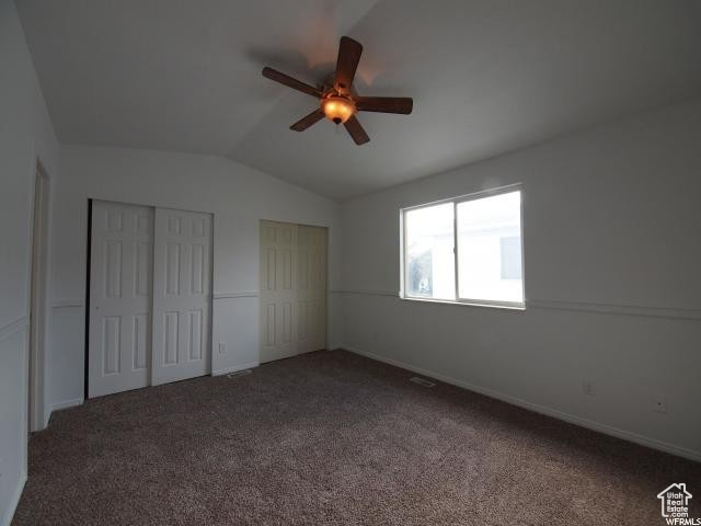 Upstairs bedroom featuring dark colored carpet, ceiling fan, two closets, and lofted ceiling