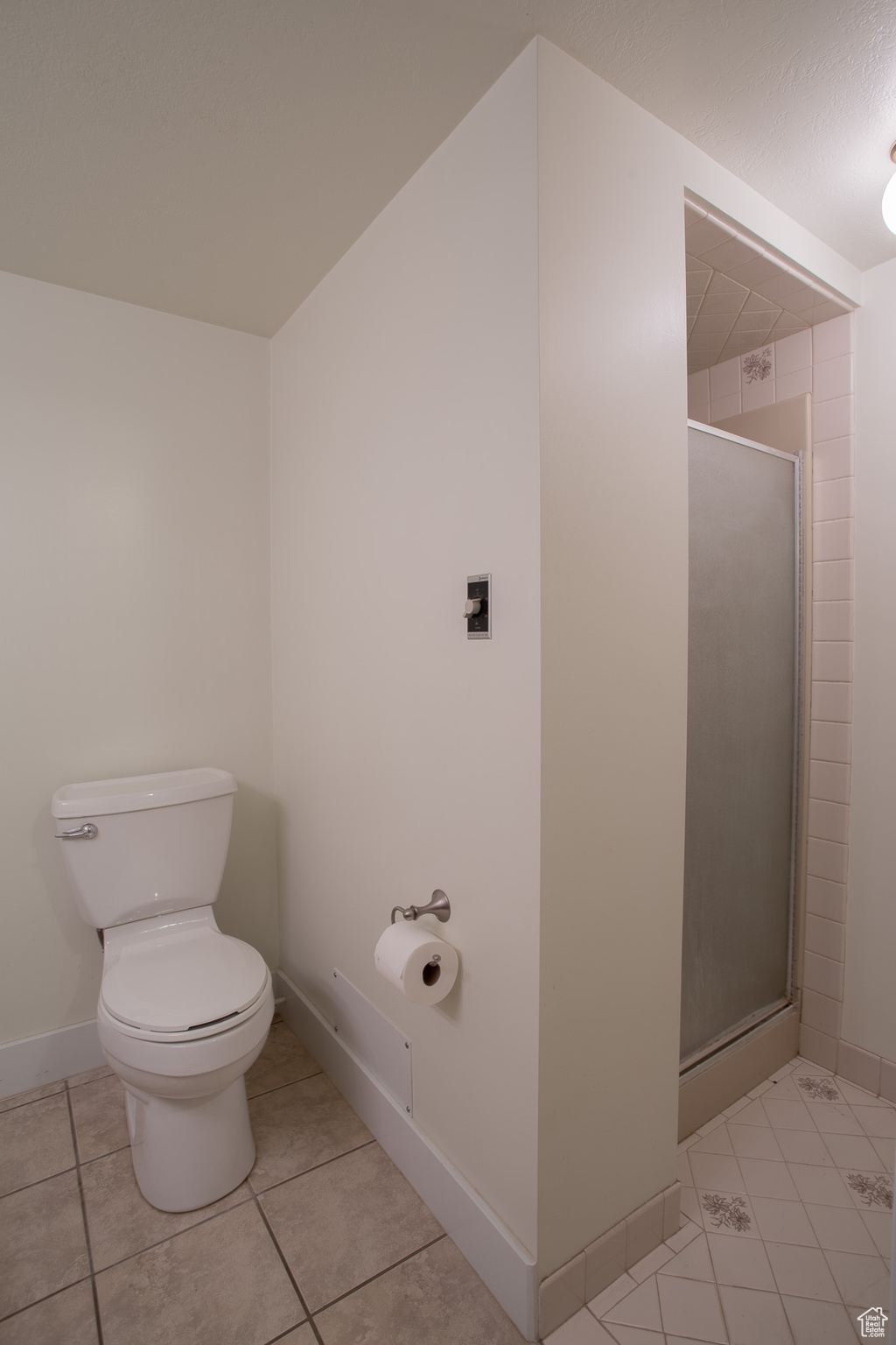 Bathroom featuring tile flooring, toilet, and a shower with shower door