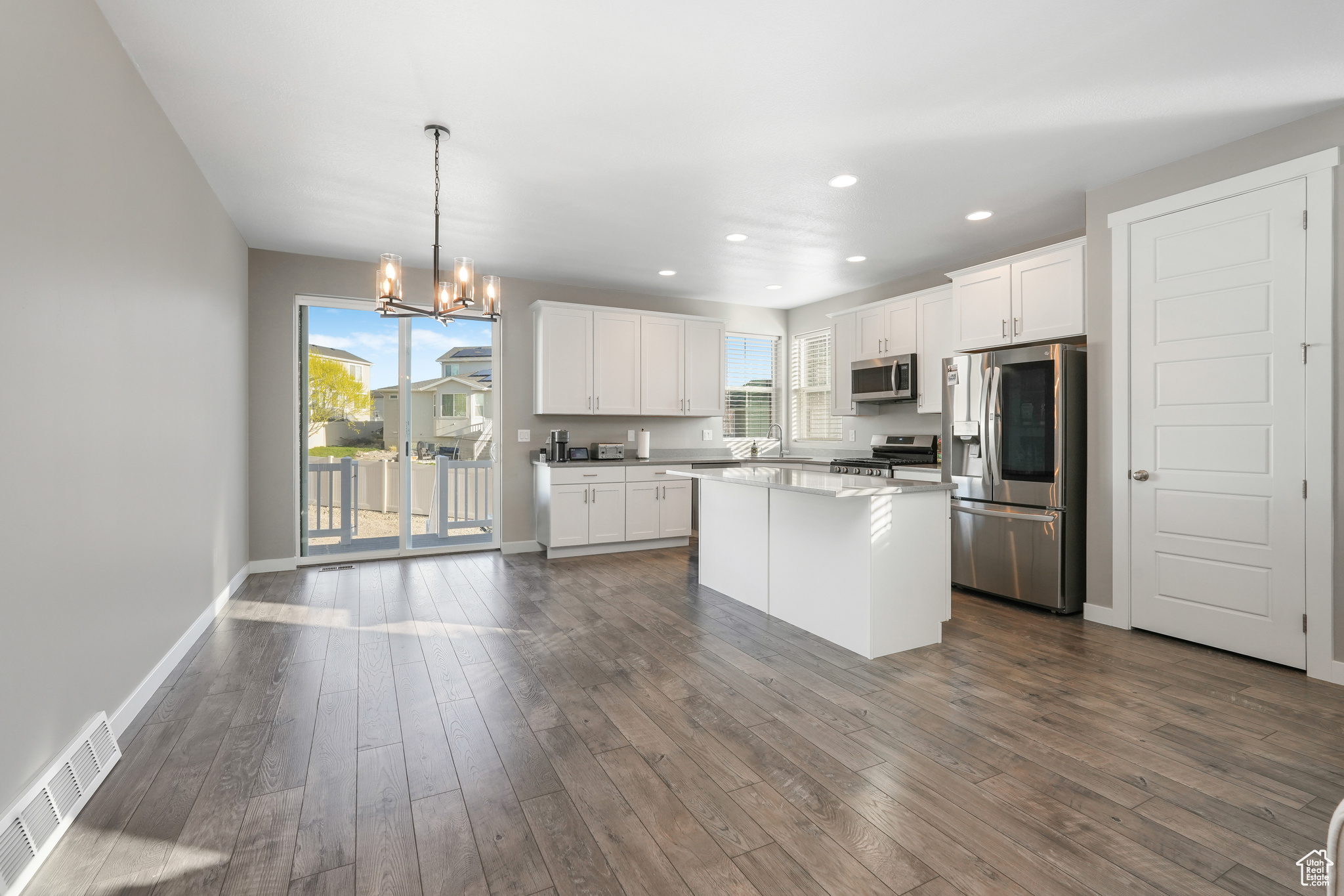 Kitchen featuring dark hardwood / wood-style flooring, stainless steel appliances, white cabinetry, and decorative light fixtures