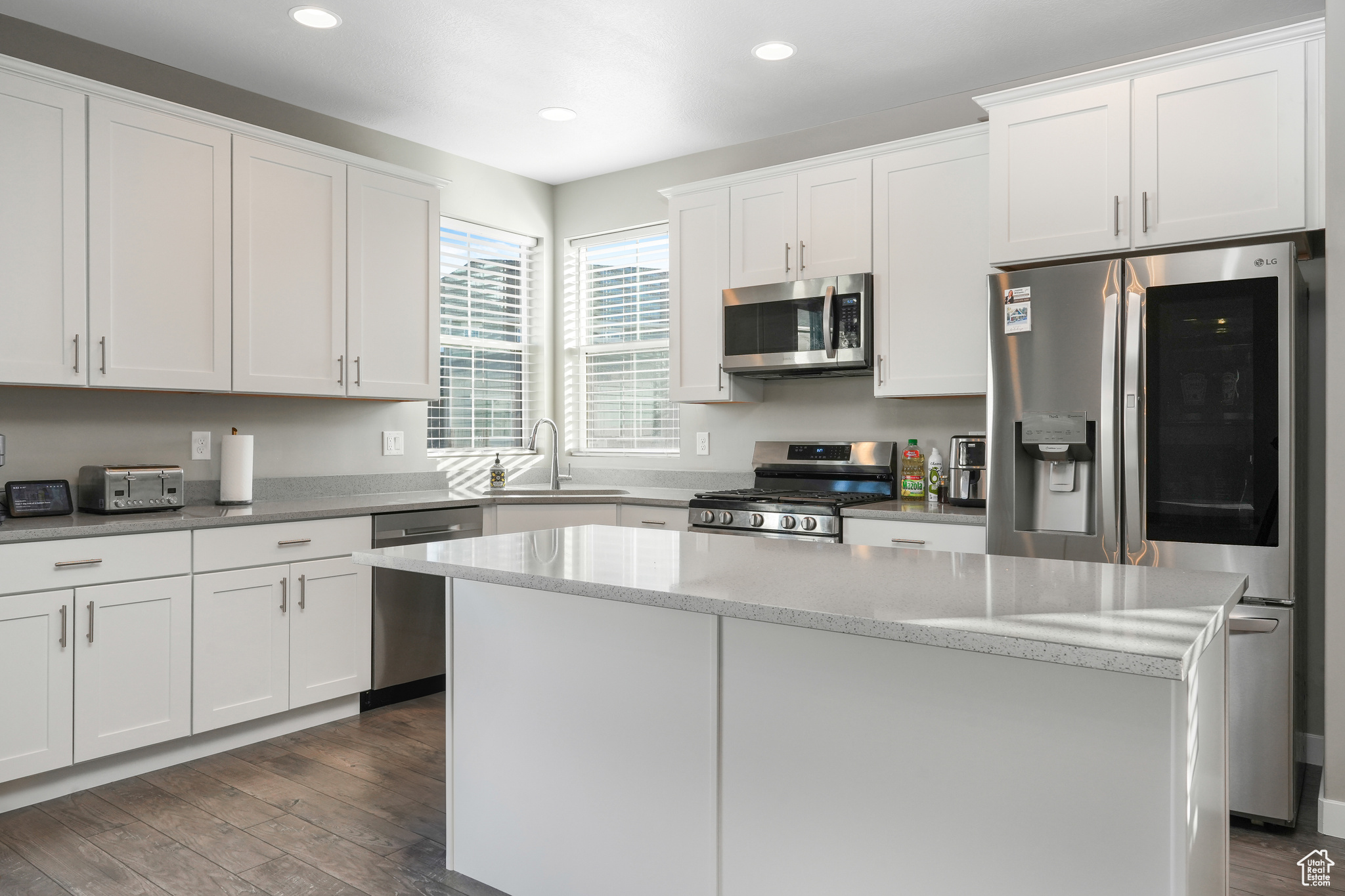 Kitchen with appliances with stainless steel finishes, a kitchen island, dark wood-type flooring, white cabinetry, and sink
