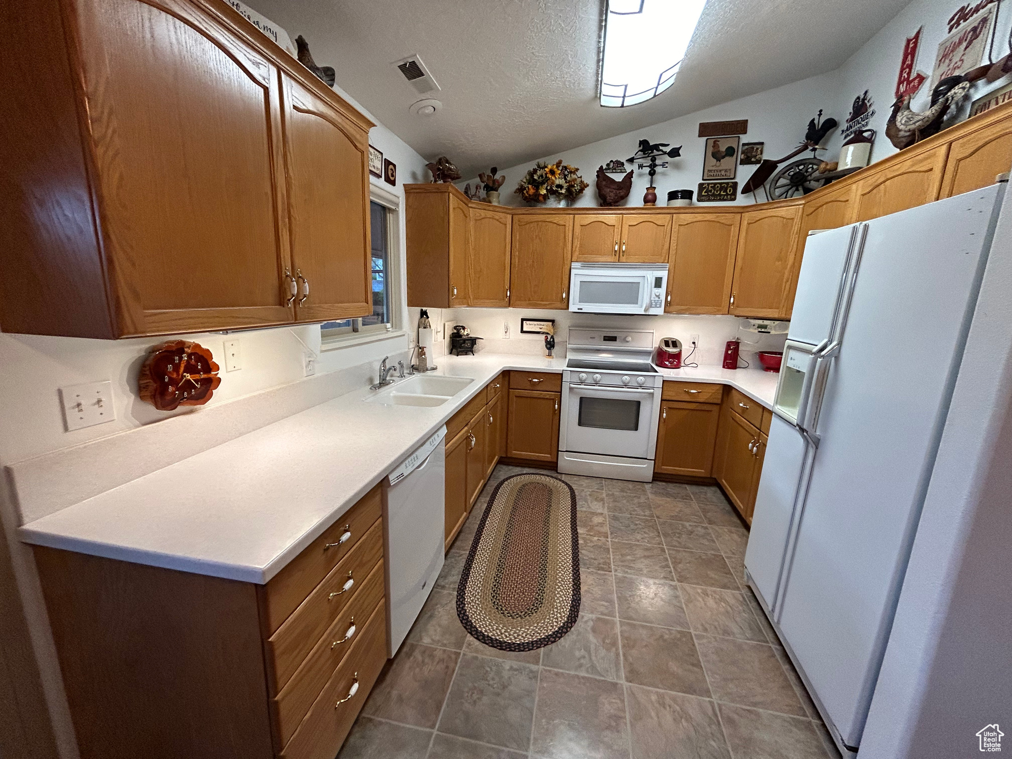 Kitchen featuring white appliances, vaulted ceiling, tile flooring, a textured ceiling, and sink