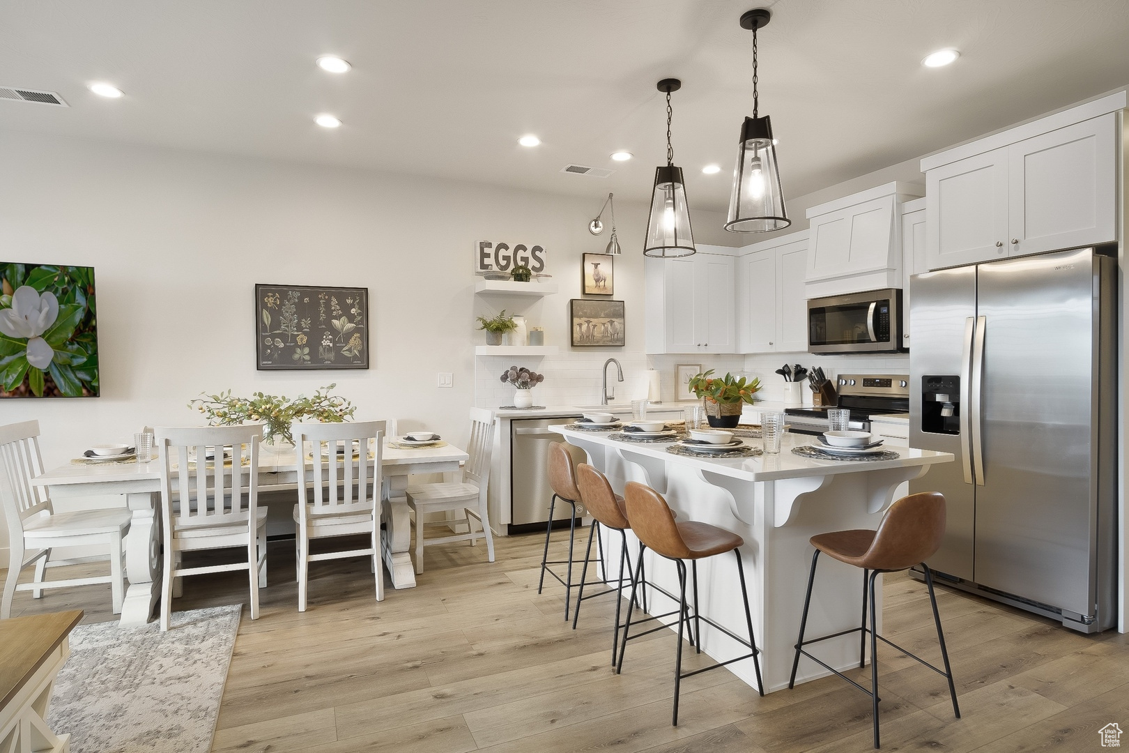 Kitchen with a kitchen island, stainless steel appliances, light hardwood / wood-style floors, white cabinets, and pendant lighting