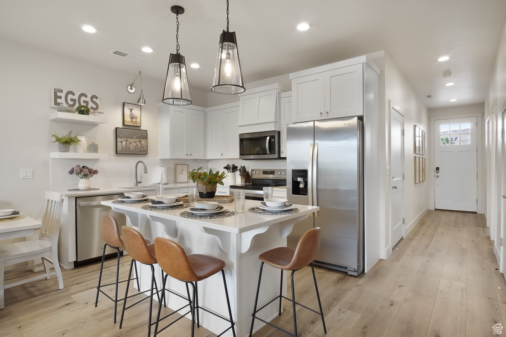 Kitchen with decorative light fixtures, white cabinets, light hardwood / wood-style flooring, stainless steel appliances, and a kitchen island