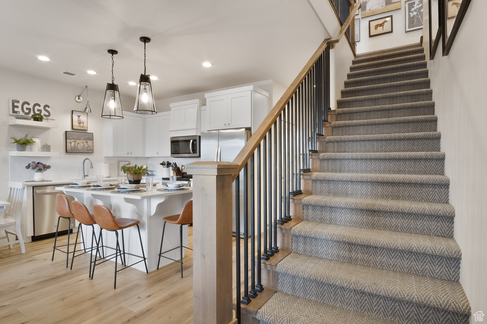 Kitchen with appliances with stainless steel finishes, a kitchen island, light hardwood / wood-style floors, white cabinetry, and pendant lighting