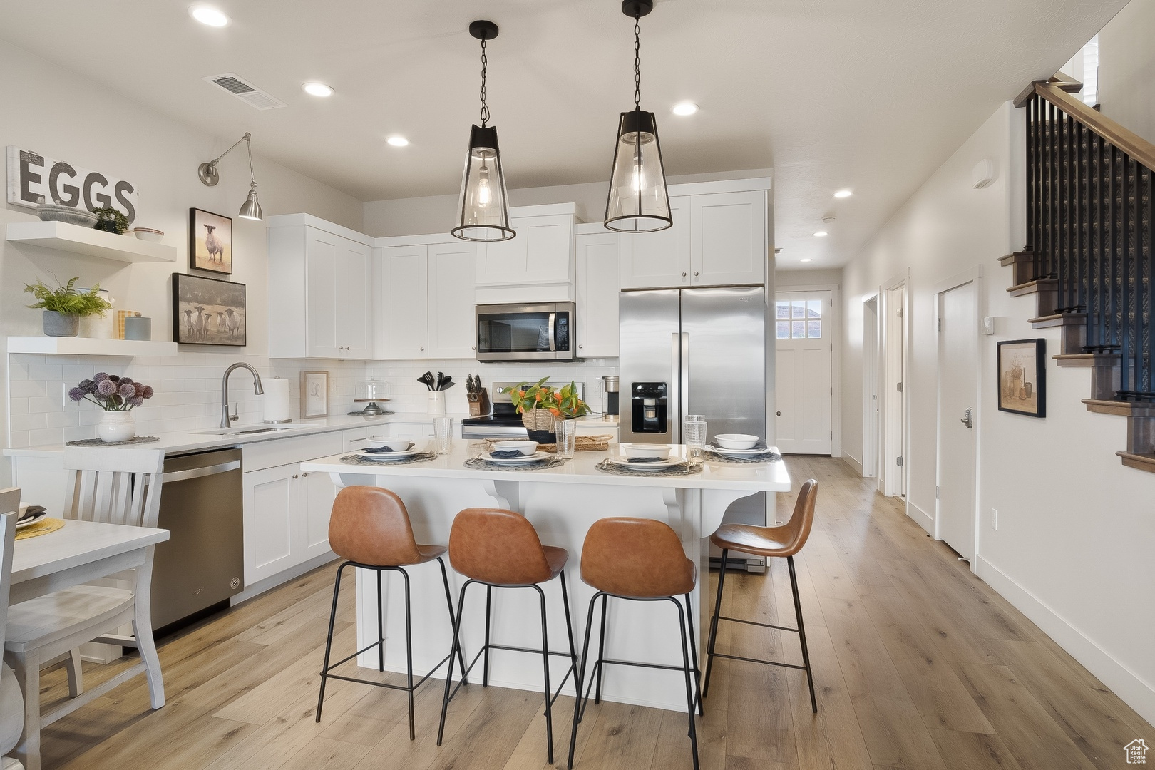 Kitchen with a center island, white cabinets, hanging light fixtures, stainless steel appliances, and light hardwood / wood-style flooring