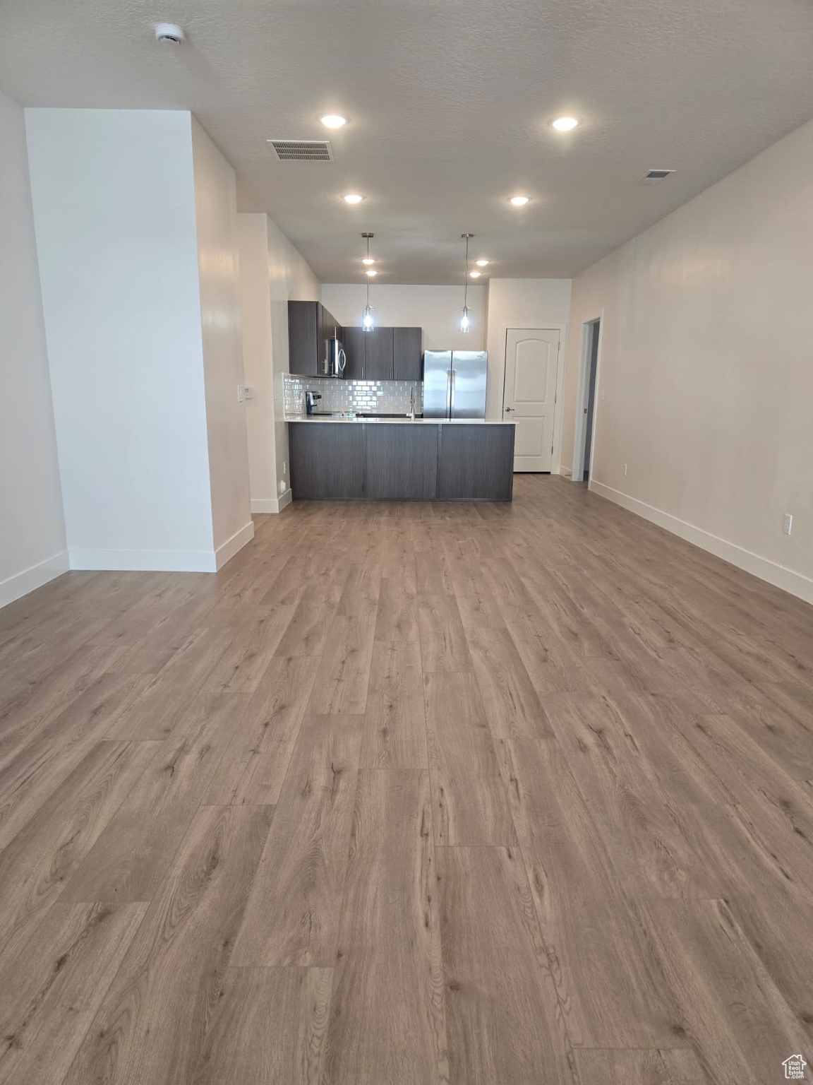 Kitchen with continuous LVP flooring throughout, stainless steel fridge, kitchen peninsula, and tasteful backsplash