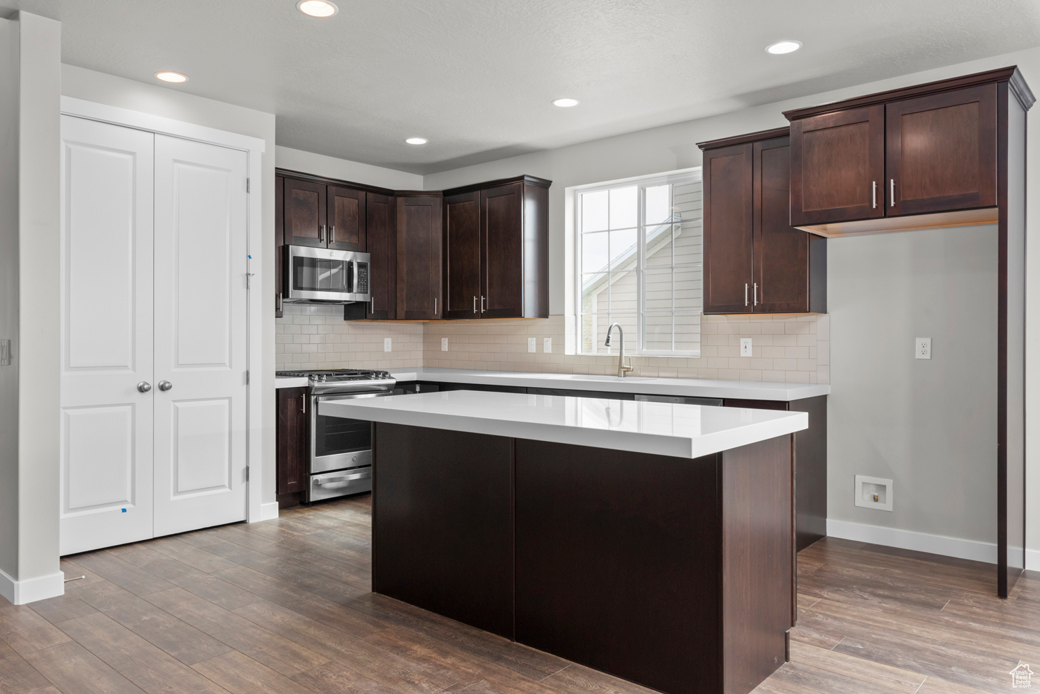 Kitchen with appliances with stainless steel finishes, a center island, hardwood / wood-style flooring, and tasteful backsplash
