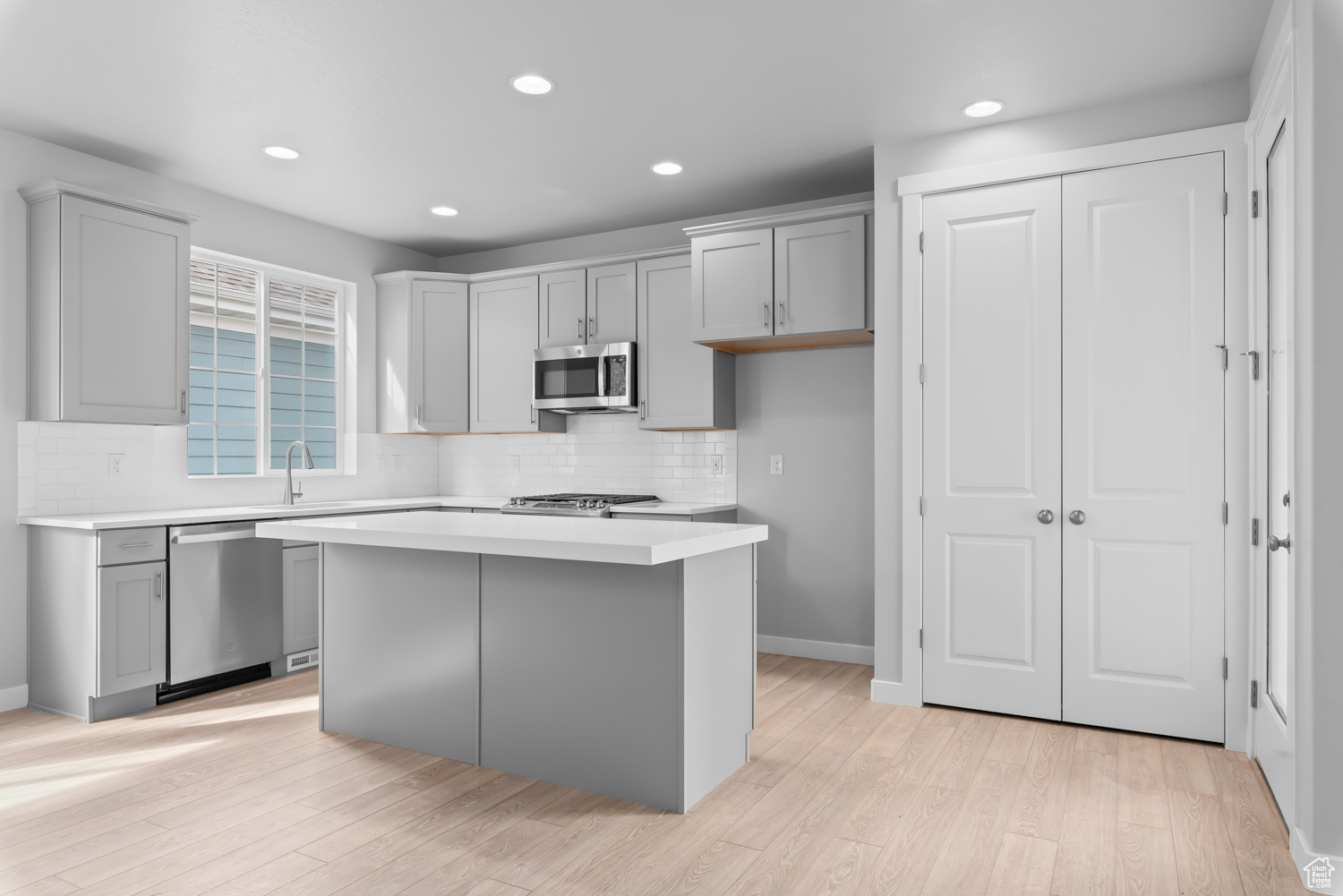 Kitchen featuring a center island, gray cabinets, appliances with stainless steel finishes, tasteful backsplash, and light hardwood / wood-style floors