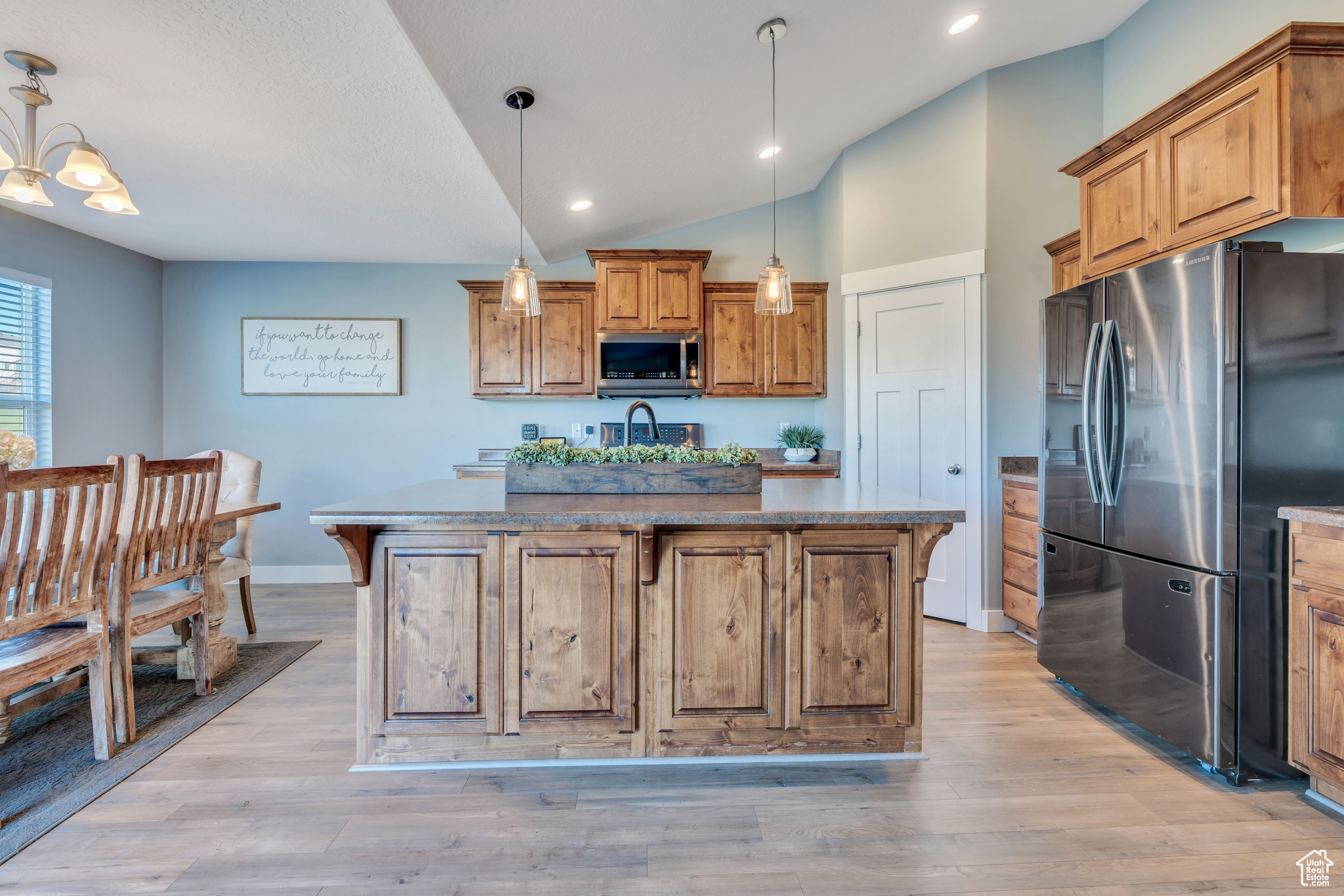Kitchen with appliances with stainless steel finishes, a breakfast bar, light hardwood / wood-style floors, decorative light fixtures, and a kitchen island with sink