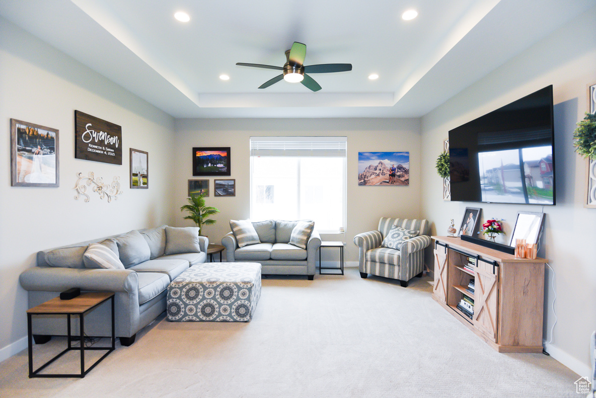 Living room with a tray ceiling, ceiling fan, and light carpet