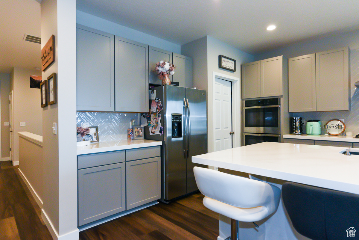 Kitchen with tasteful backsplash, gray cabinets, dark wood-type flooring, and stainless steel appliances