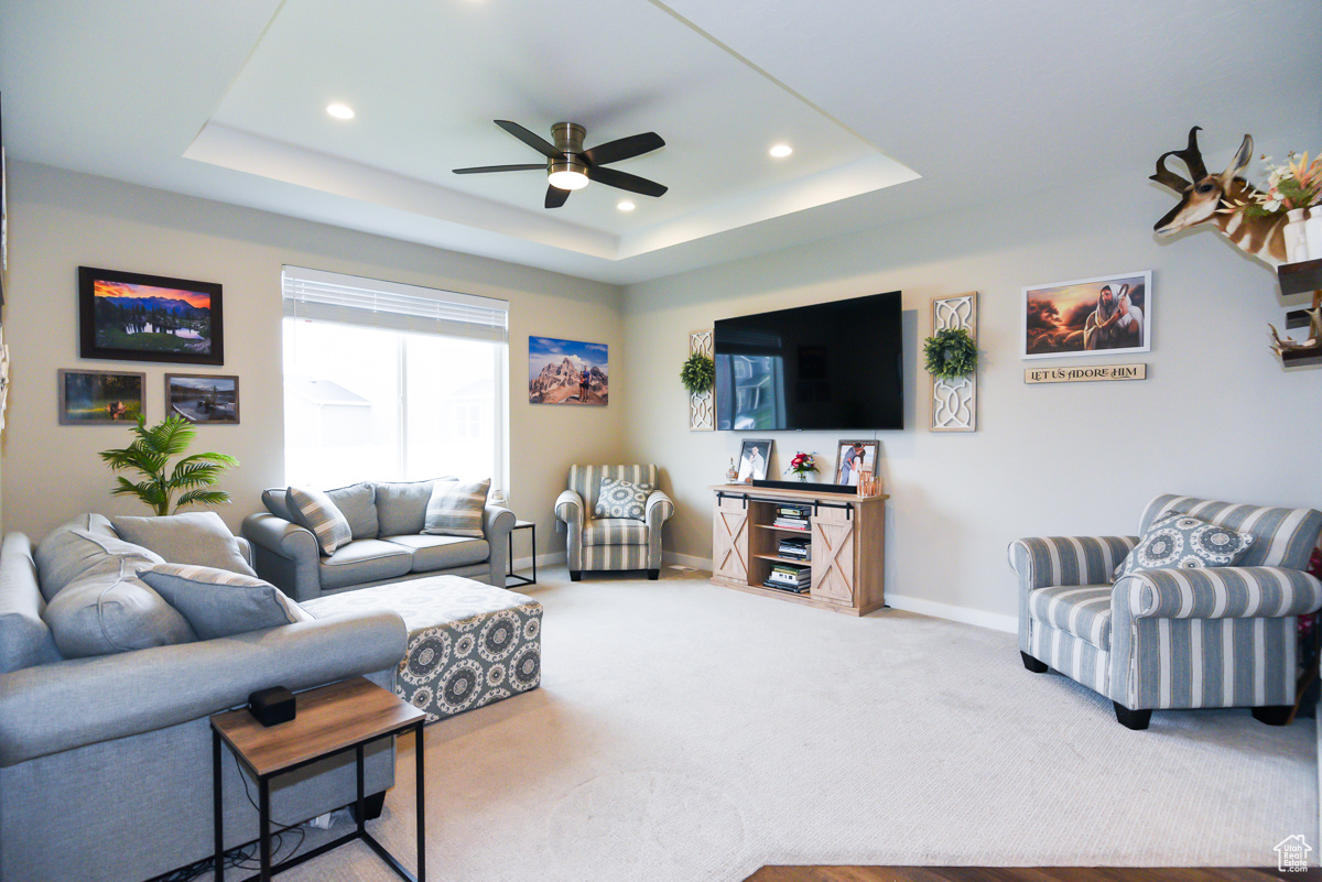 Carpeted living room featuring ceiling fan and a raised ceiling