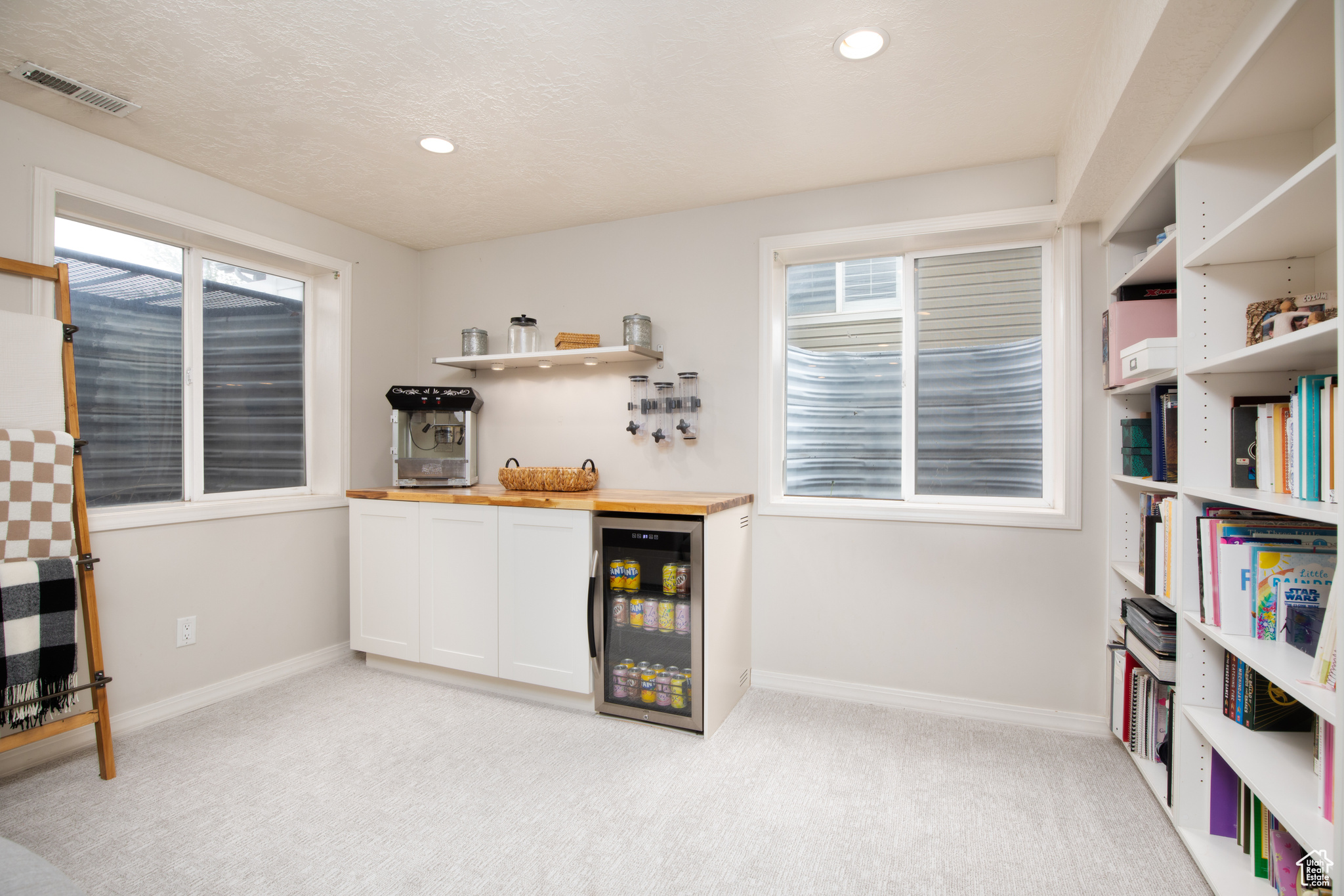Interior space with plenty of natural light, light colored carpet, white cabinetry, and beverage cooler