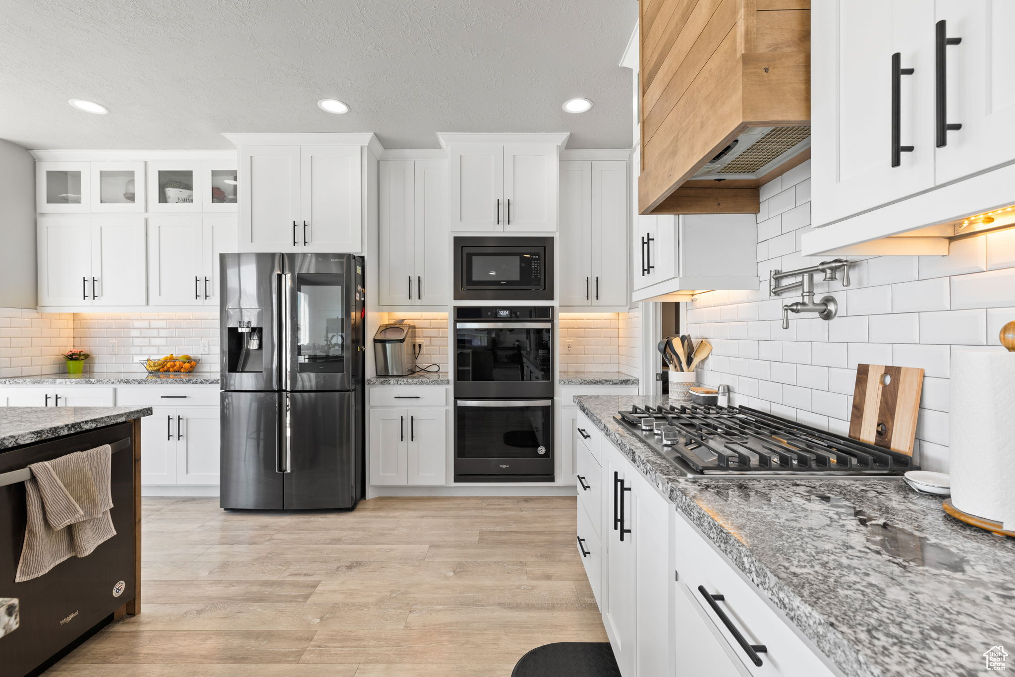 Kitchen featuring backsplash, appliances with stainless steel finishes, custom exhaust hood, and white cabinets