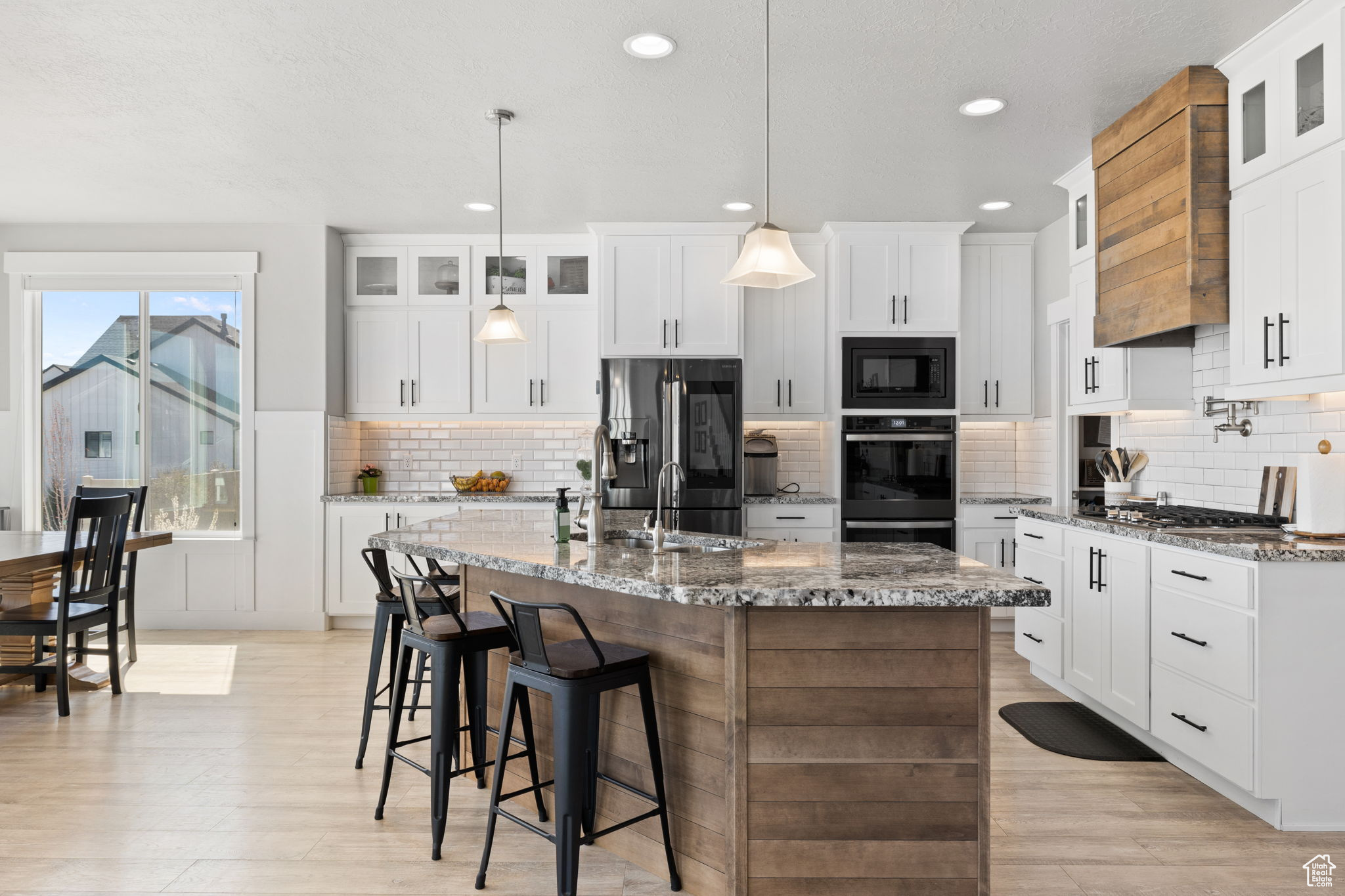 Kitchen with white cabinets, backsplash, an island with sink, and black appliances